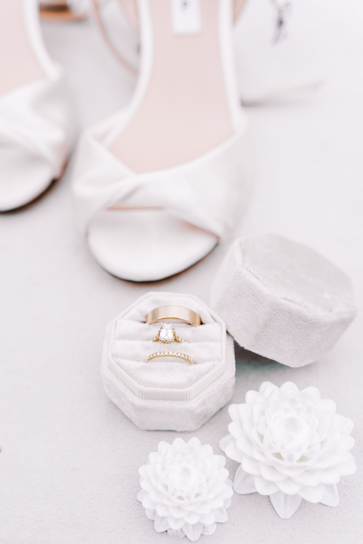 White wedding rings and delicate floral decorations arranged on a light pink surface.