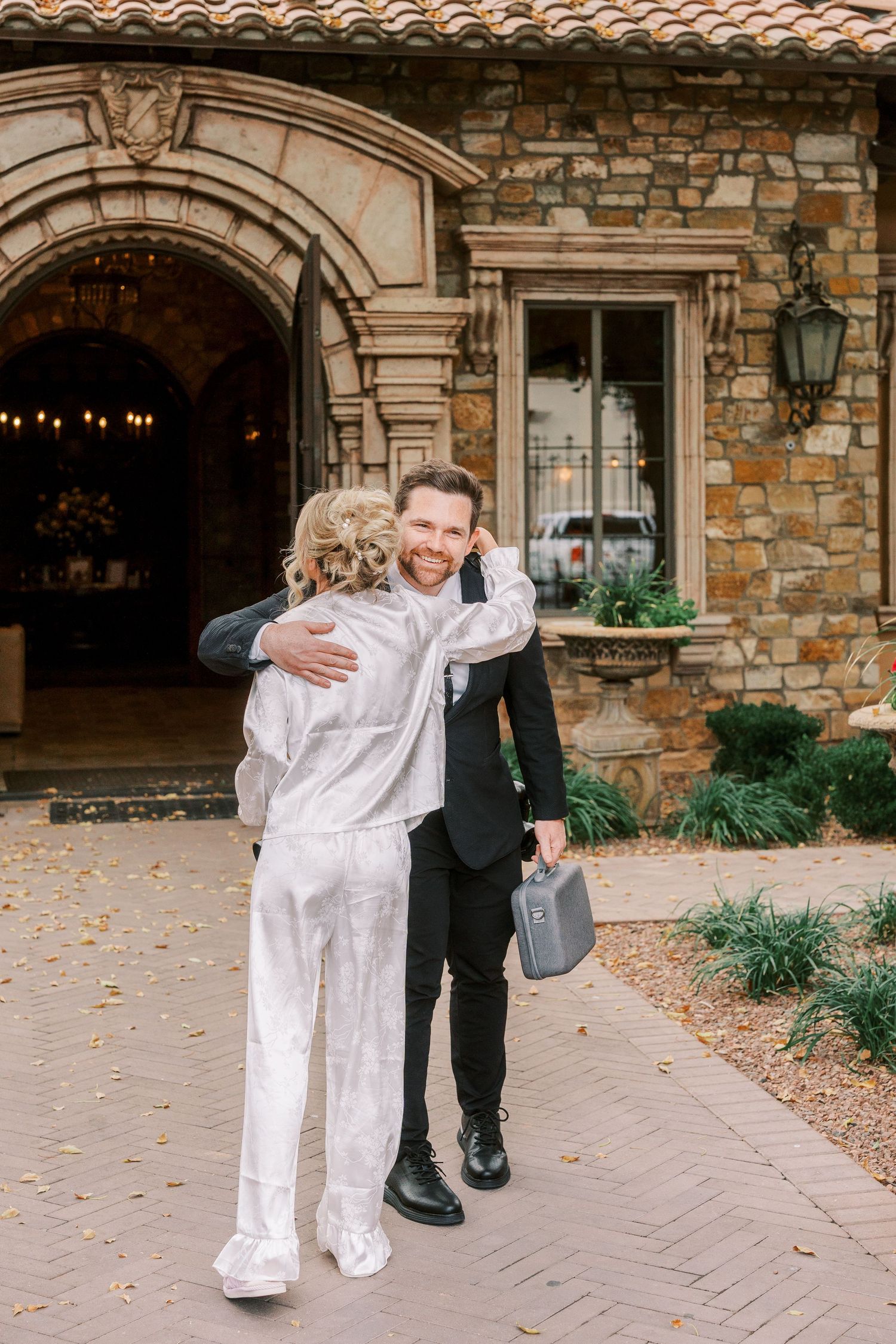 A couple shares a joyful dance moment on a stone patio with autumn leaves scattered around them.