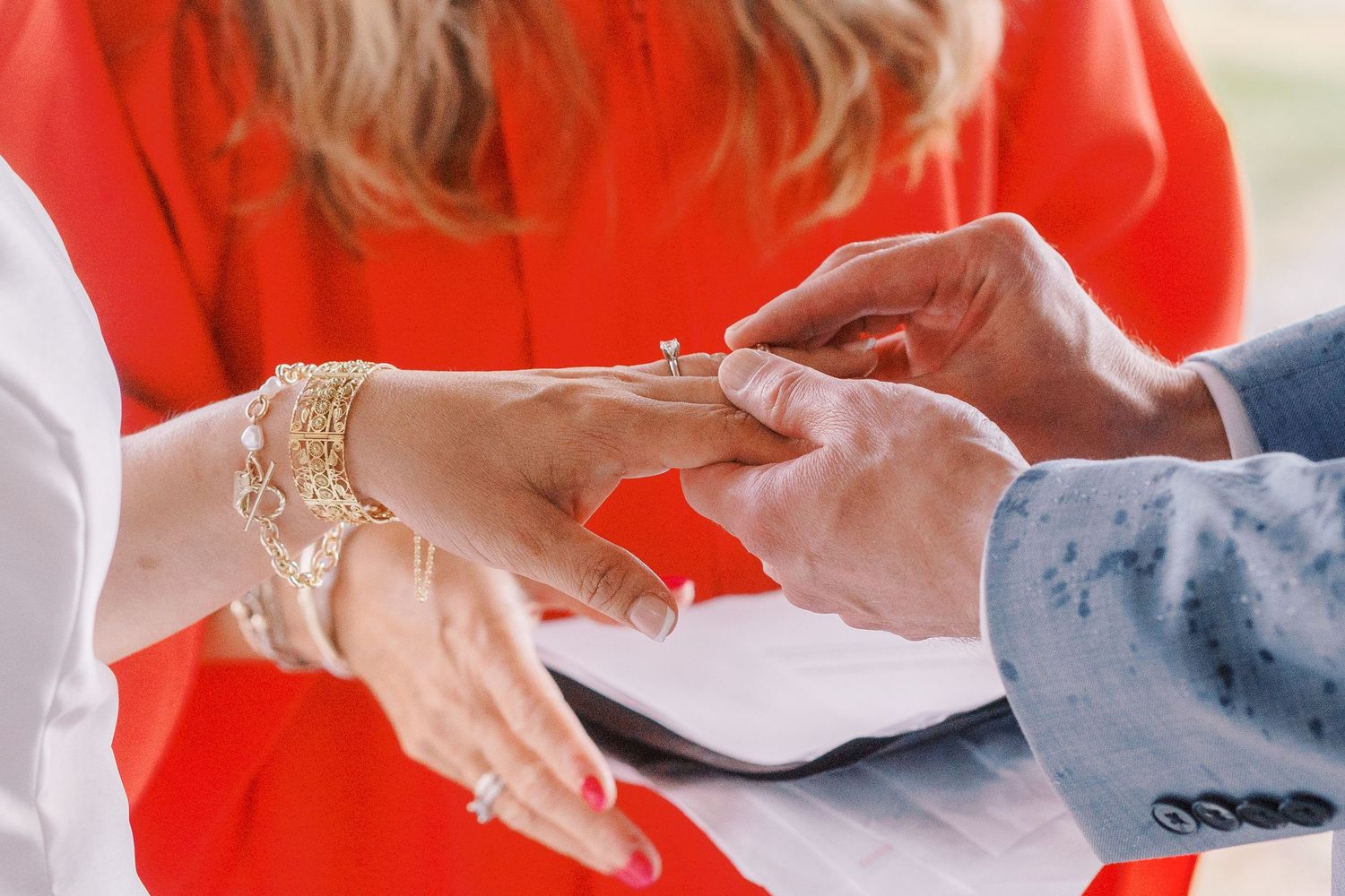 Close-up hands wearing blue latex gloves writing on medical paperwork at a desk with red backdrop.