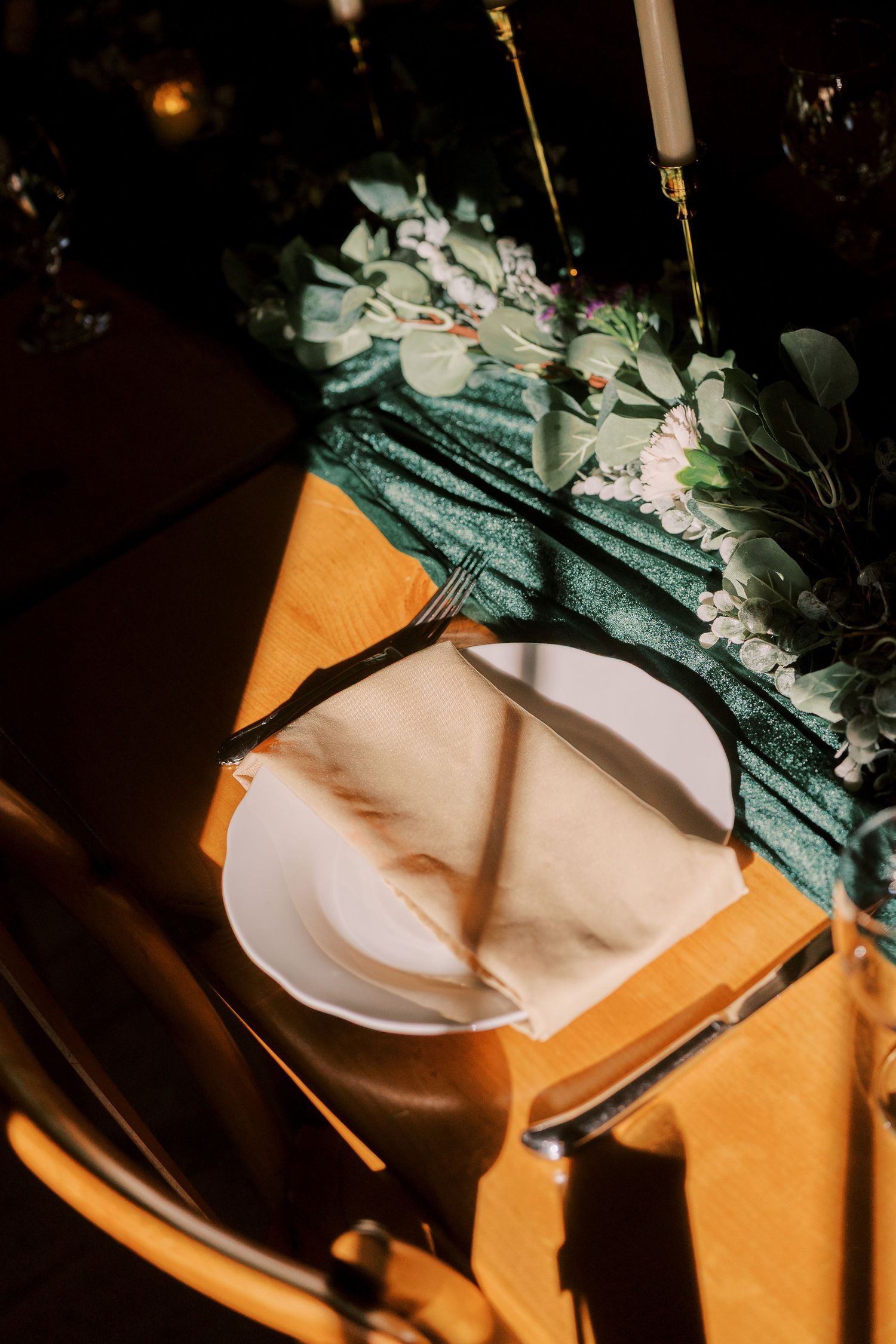 White plates and floral arrangements cast dramatic shadows on an orange surface in moody lighting.