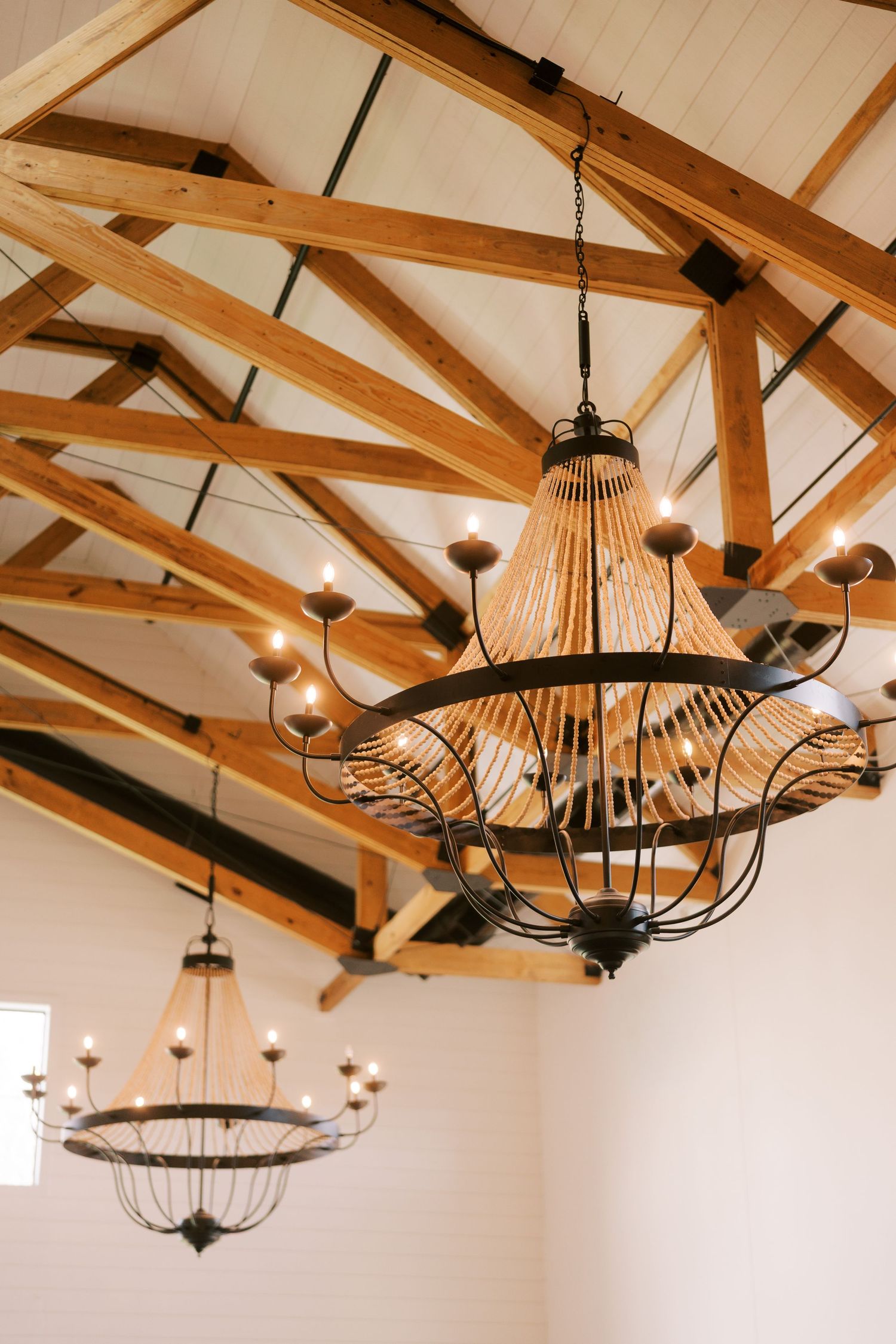 Modern rustic pendant light fixtures with metal frames hang from exposed wooden ceiling beams in a vaulted room.