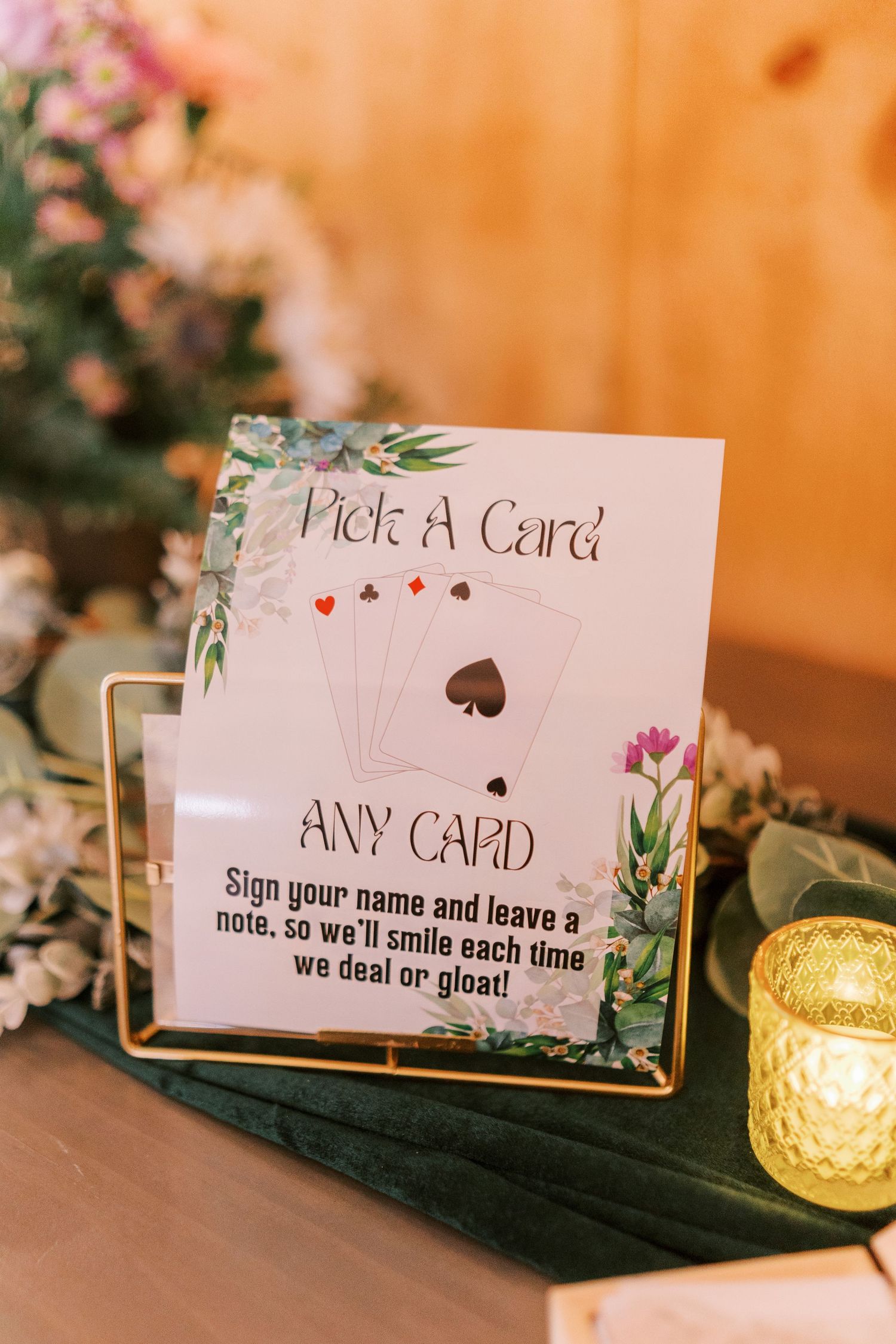 Wedding reception sign cards display with 'Pick A Card' text and floral decorations on a table with glowing candle holders.
