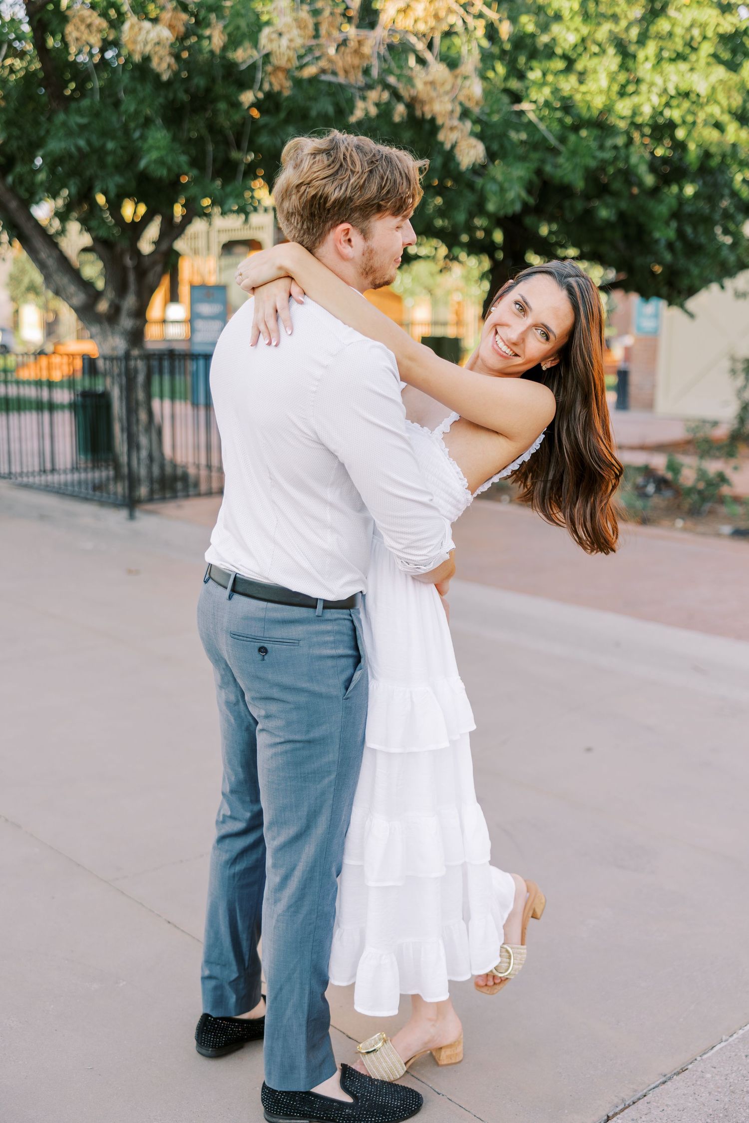 Romantic couple dancing together outdoors in a park setting with golden sunlight filtering through trees.