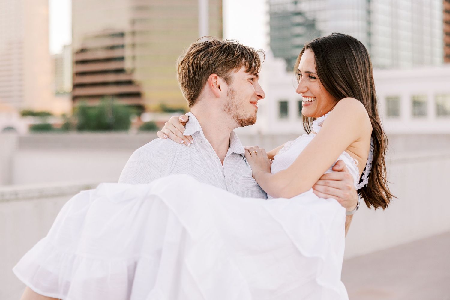 A couple in white outfits shares playful and romantic moments during their engagement session.