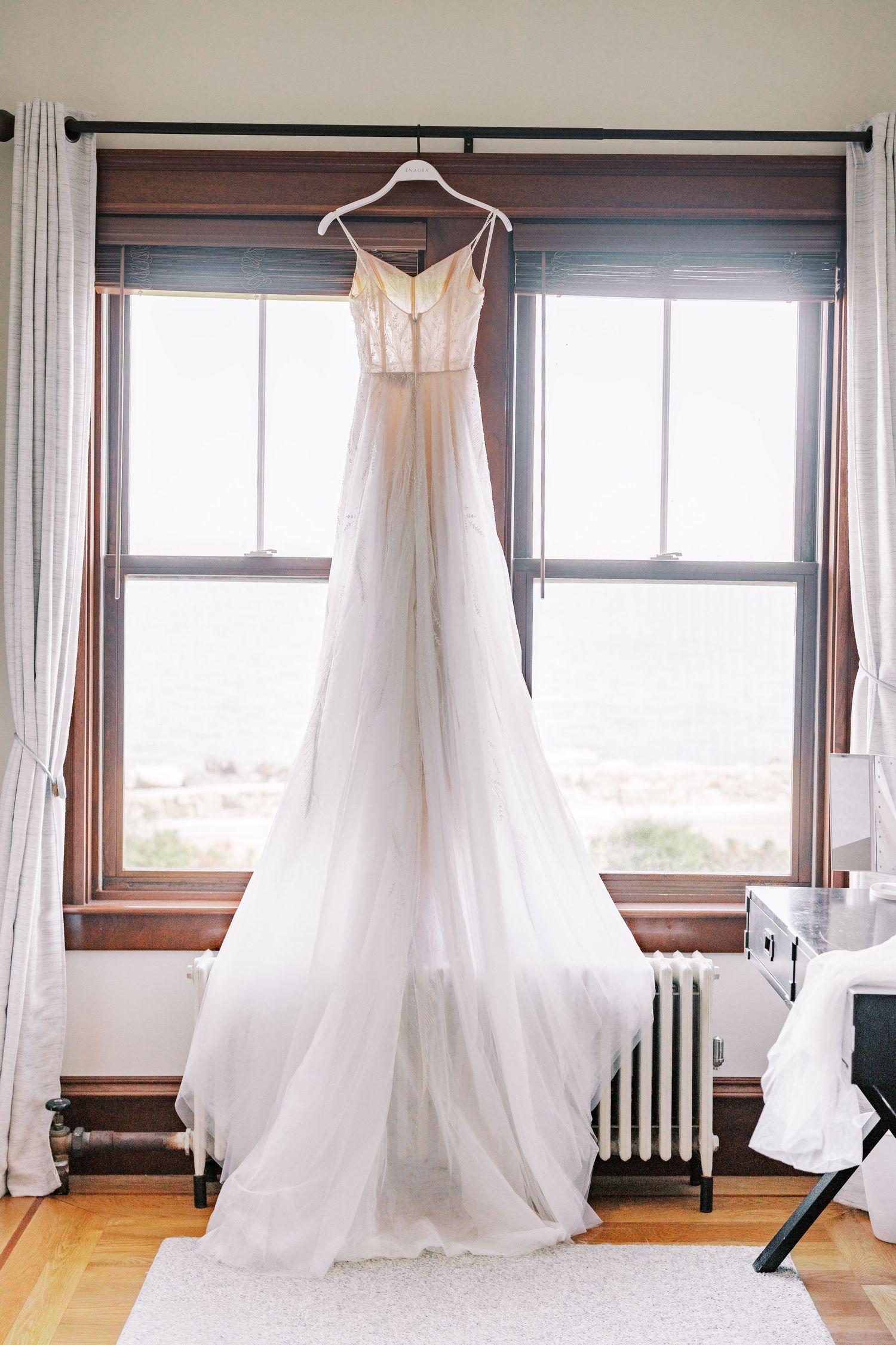White wedding dresses hang elegantly by windows in a sunlit dressing room.