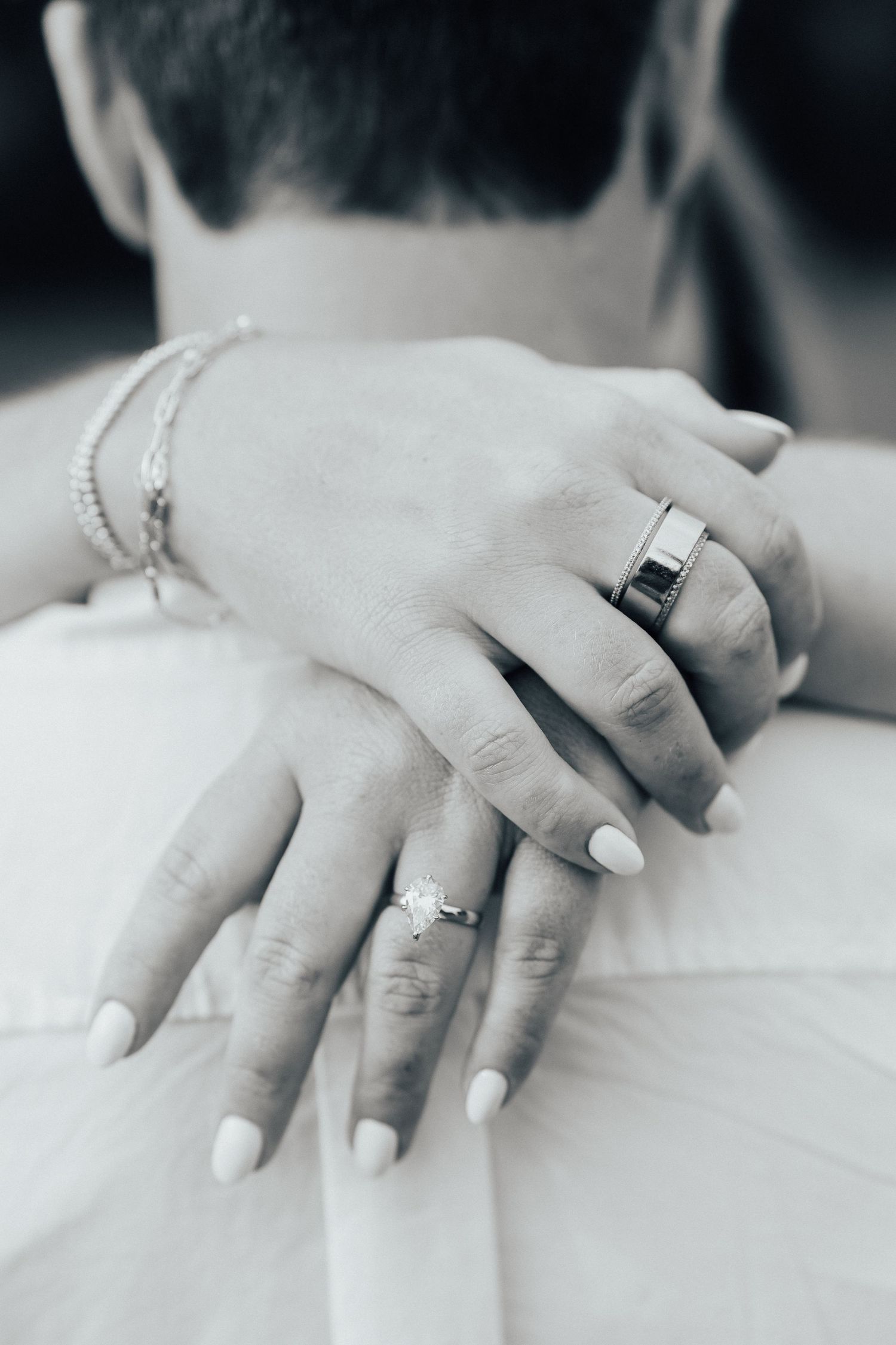 Close-up black and white photo of hands with wedding rings and white nail polish.