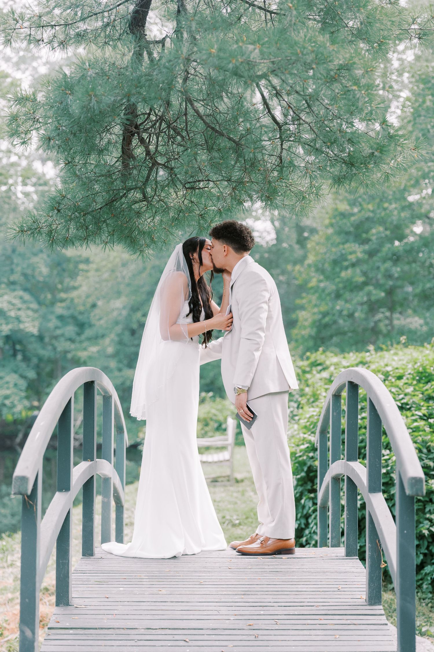 Couple shares romantic moment on white bridge surrounded by lush greenery.
