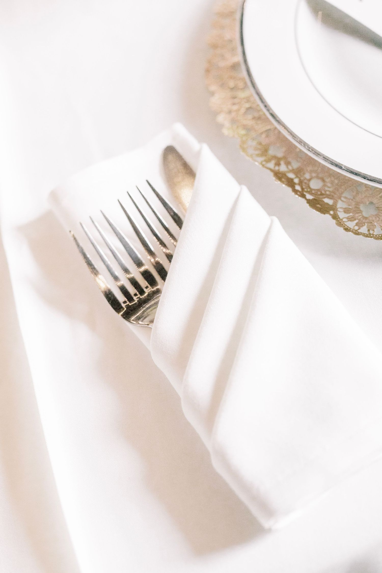 Elegant place setting with silverware wrapped in white napkin and gold-rimmed plate.