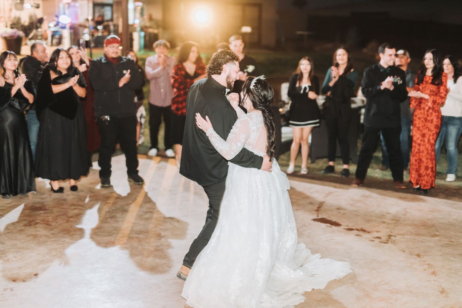 A couple shares their first dance at a wedding reception while guests gather around to watch and celebrate.