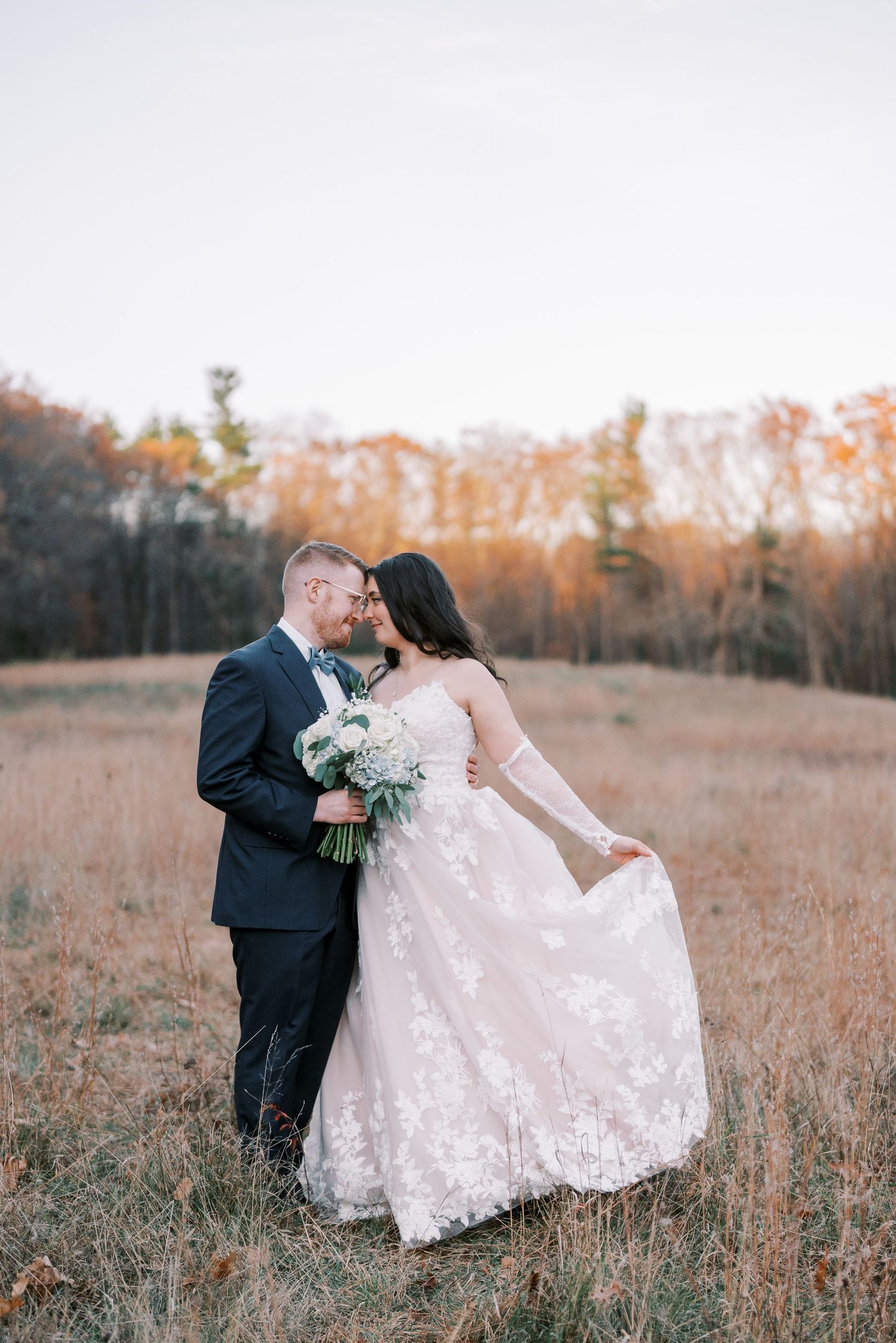 A couple shares a romantic moment in a golden autumn field while wearing wedding attire at sunset.