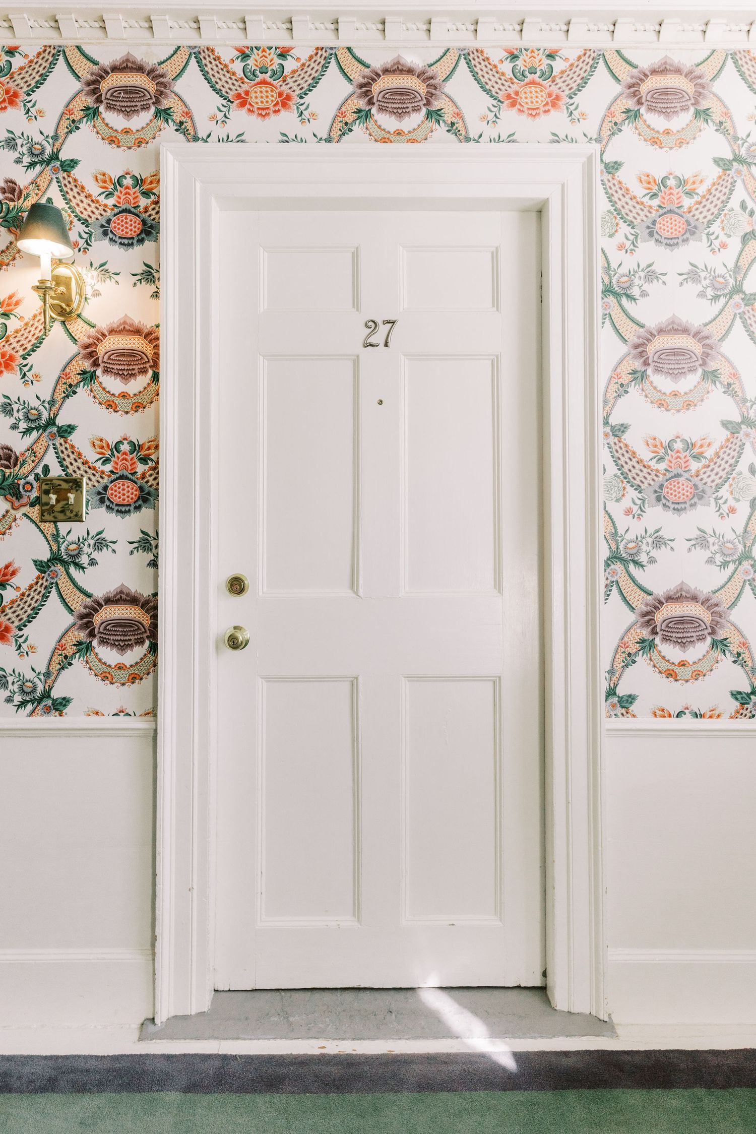 White door numbered 27 with decorative floral wallpaper featuring coral and green botanical patterns.
