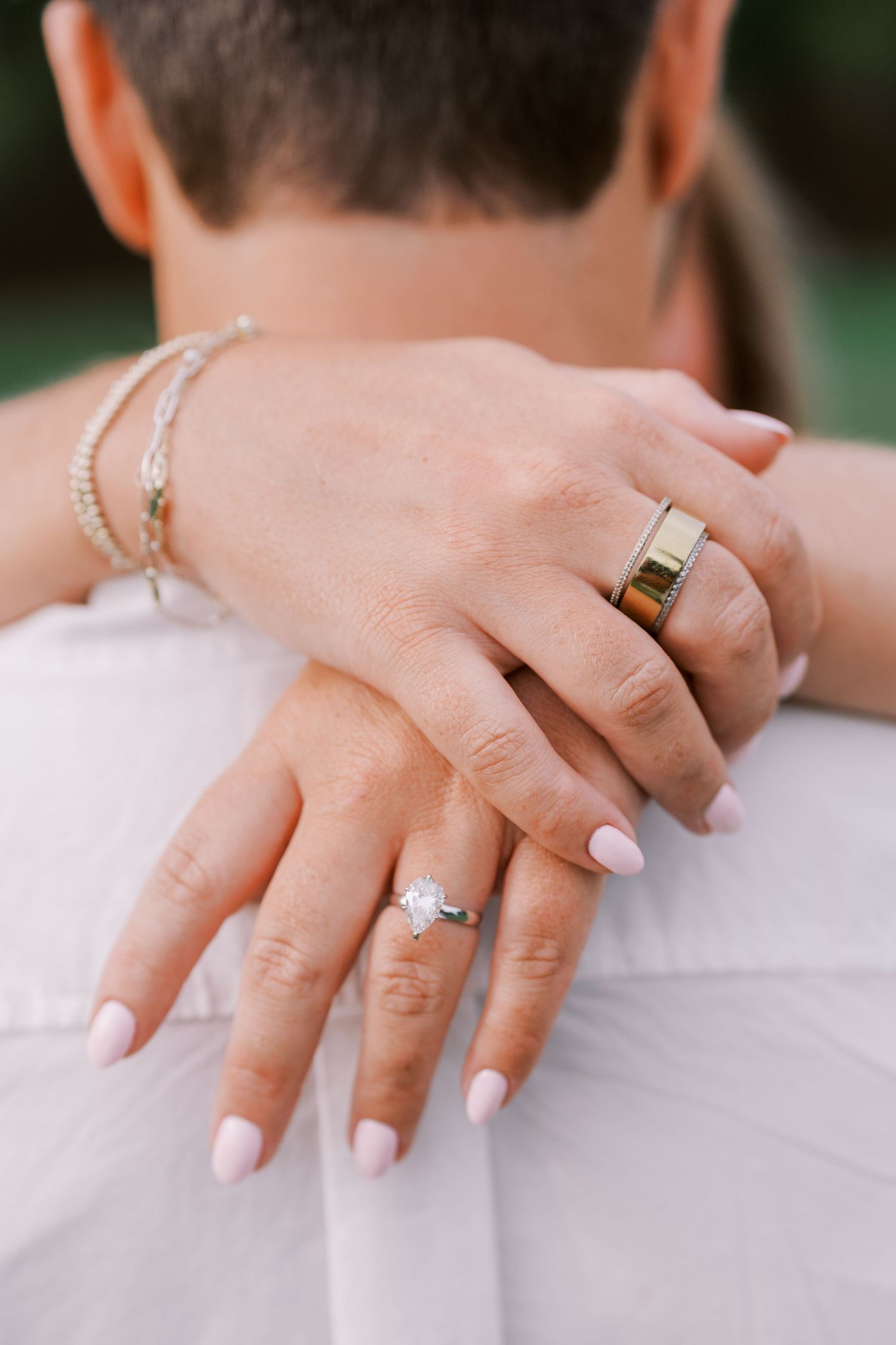 Close-up view of hands wearing elegant engagement and wedding rings with manicured nails against a white background.