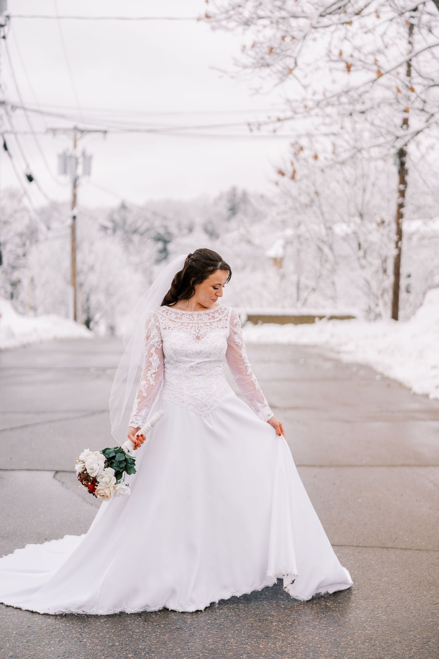 Bride in long-sleeved lace wedding gown twirling on a snow-covered winter street.