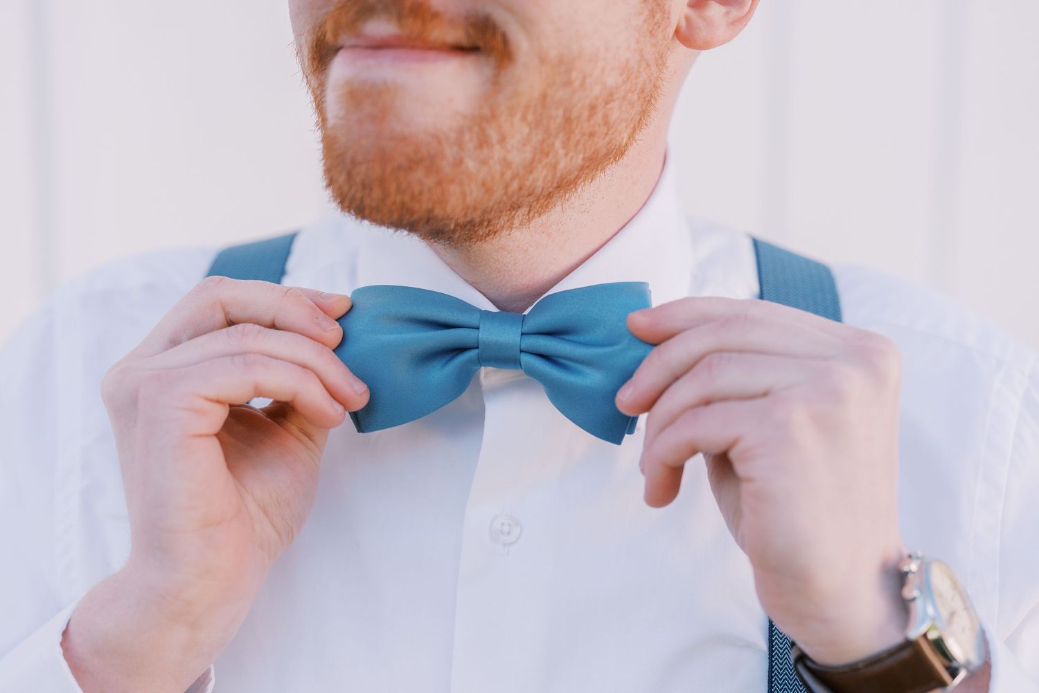 A person adjusts a light blue bowtie while wearing a white dress shirt.