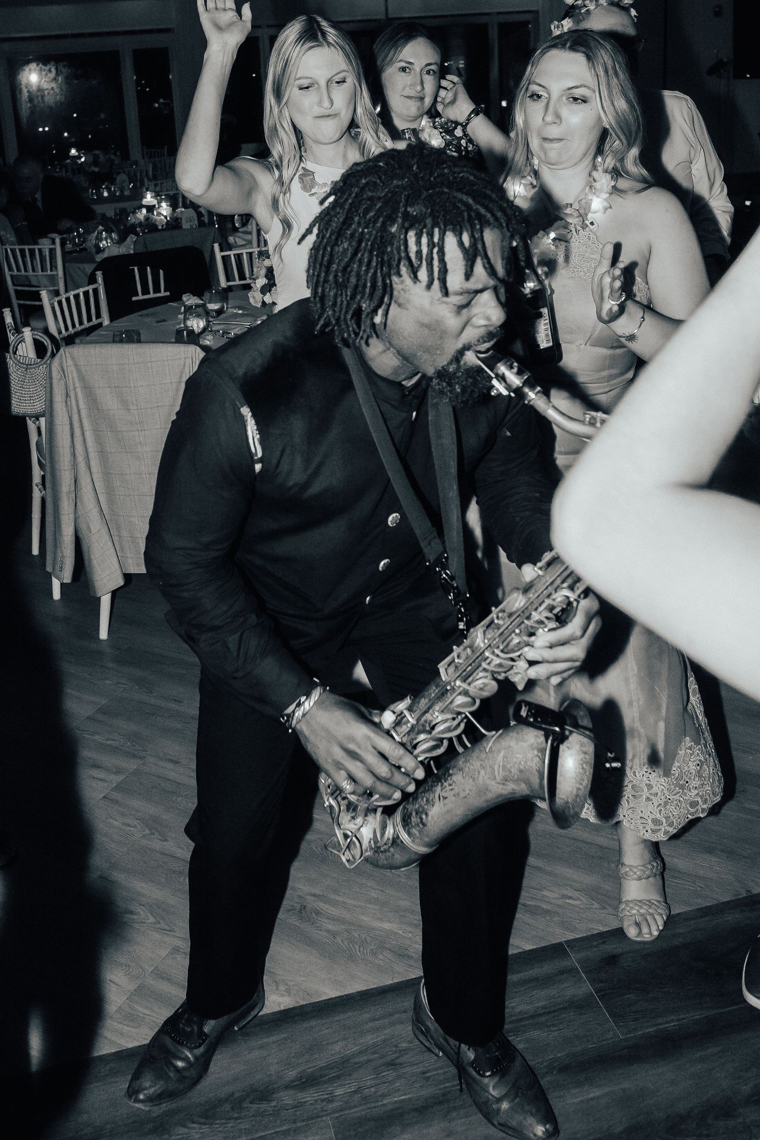 Musician in black plays saxophone on dance floor while performing for wedding guests during reception celebration.