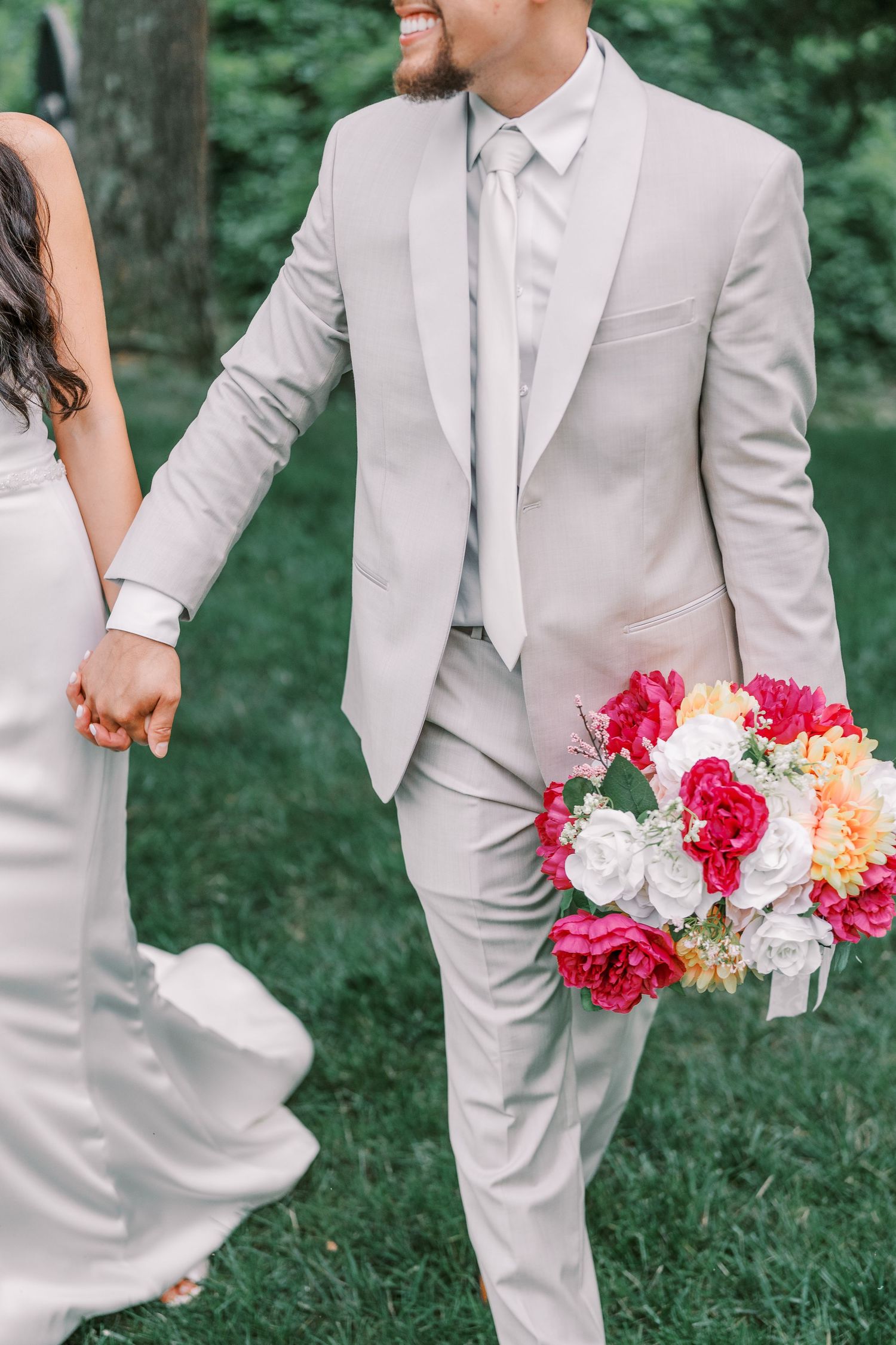Stylish wedding party wearing light gray suits holding vibrant pink and white floral bouquets in an outdoor garden setting.