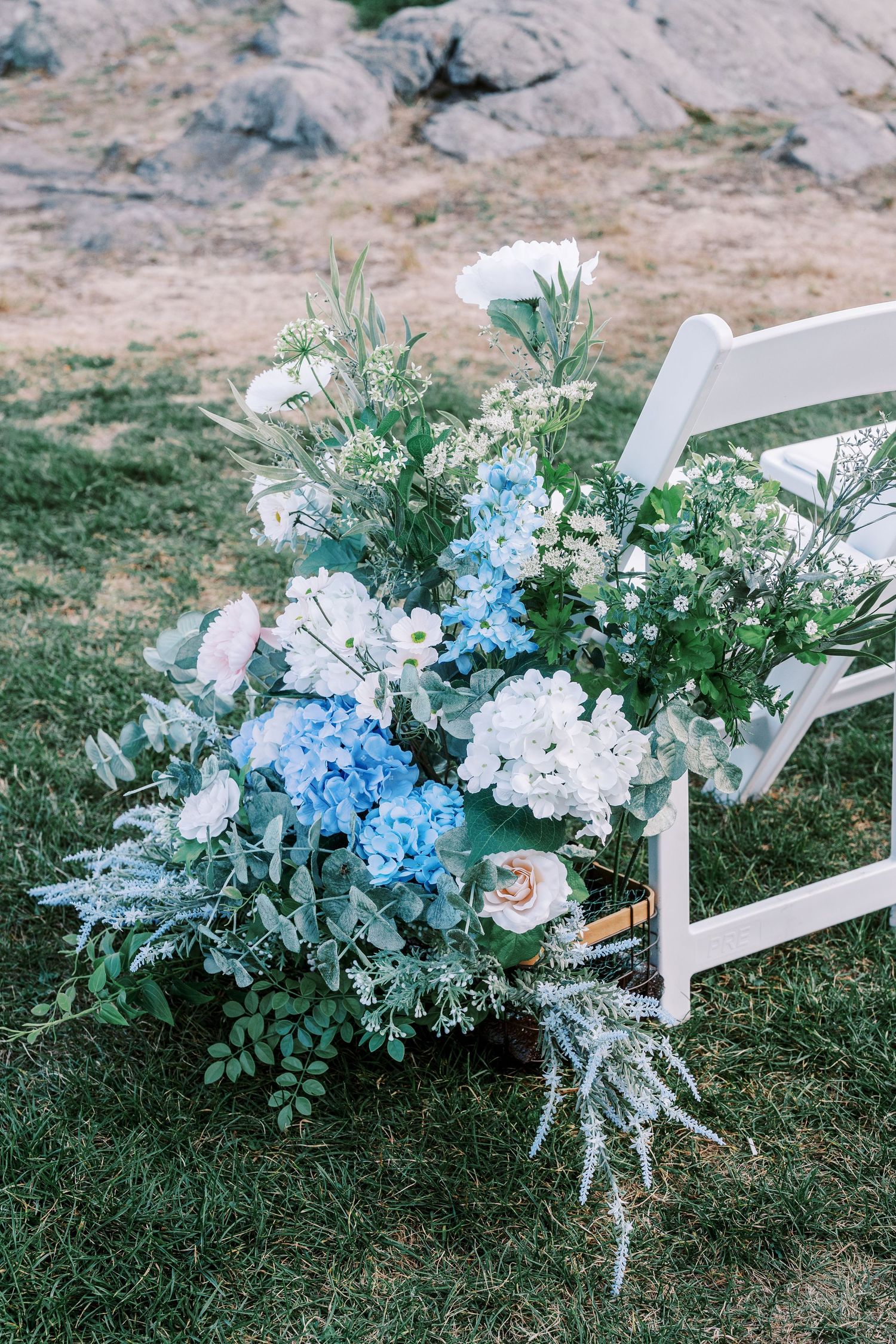 Beautiful wedding floral arrangement with white and blue hydrangeas decorating a white ceremony chair on grass.