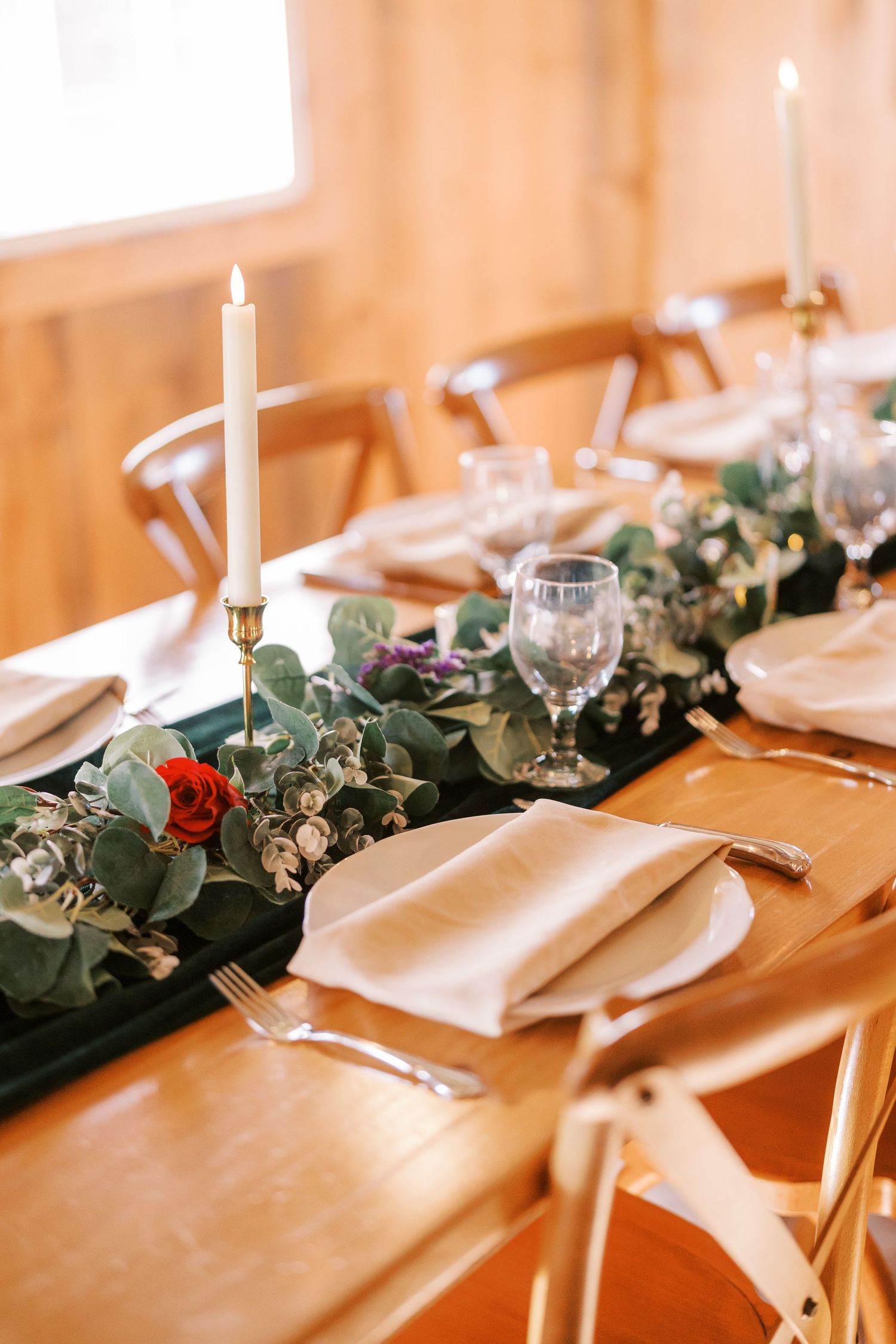 Elegant wedding table settings with white candles, eucalyptus garland, and white napkins on a wooden table.