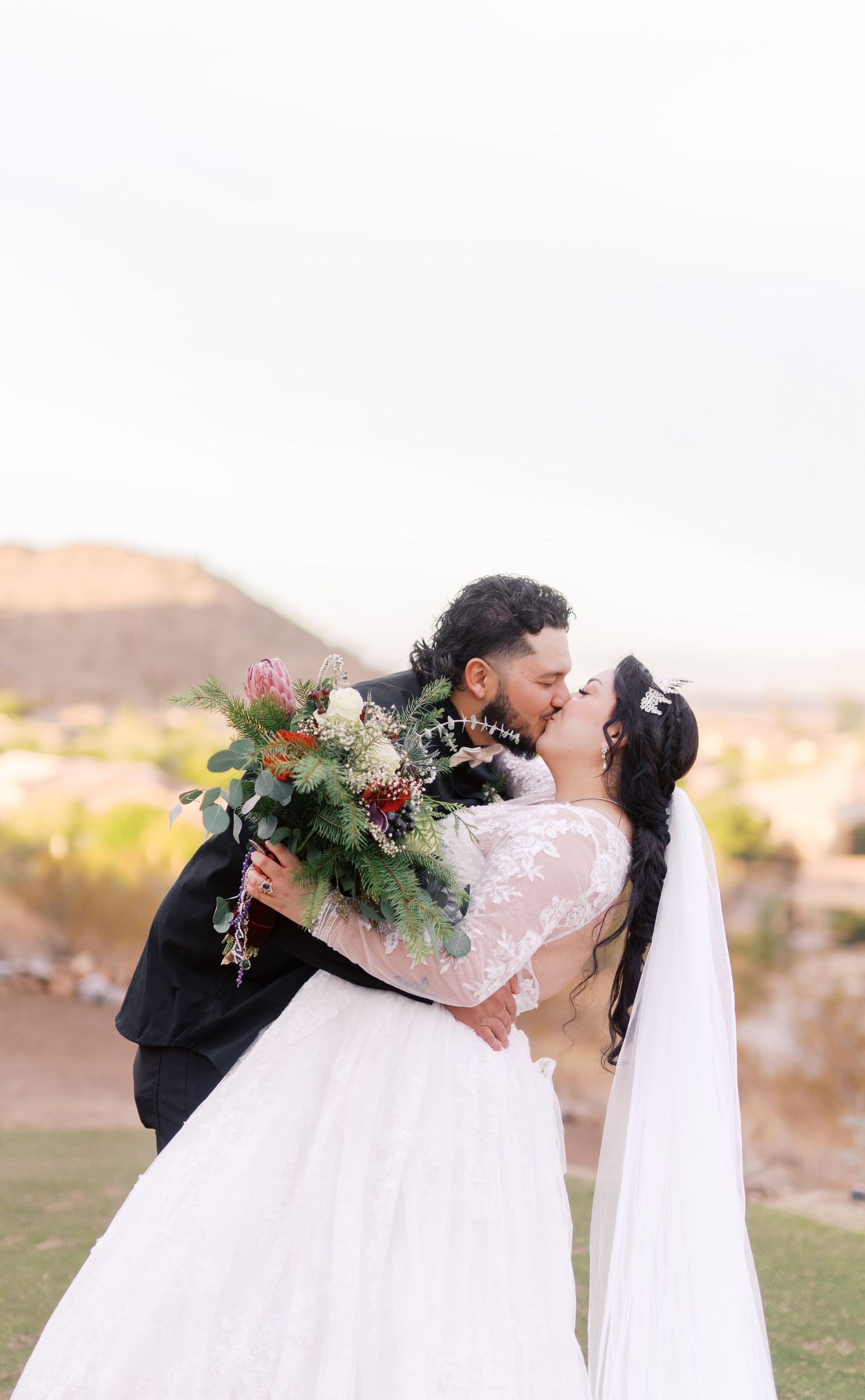 A romantic moment between newlyweds sharing a kiss in an outdoor garden setting with mountain vistas in the background.