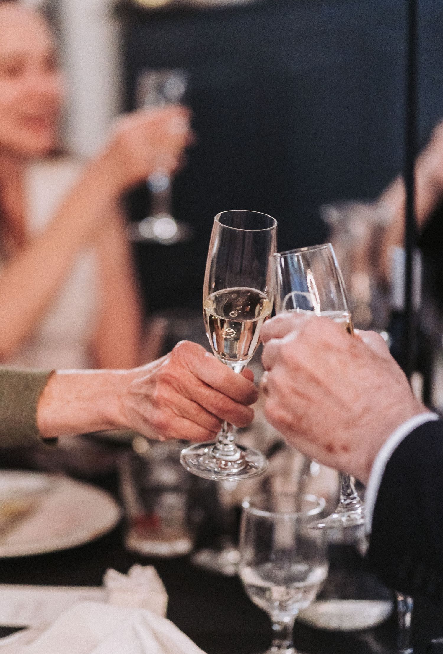 Two people clink wine glasses together in an elegant restaurant setting during a dining celebration.