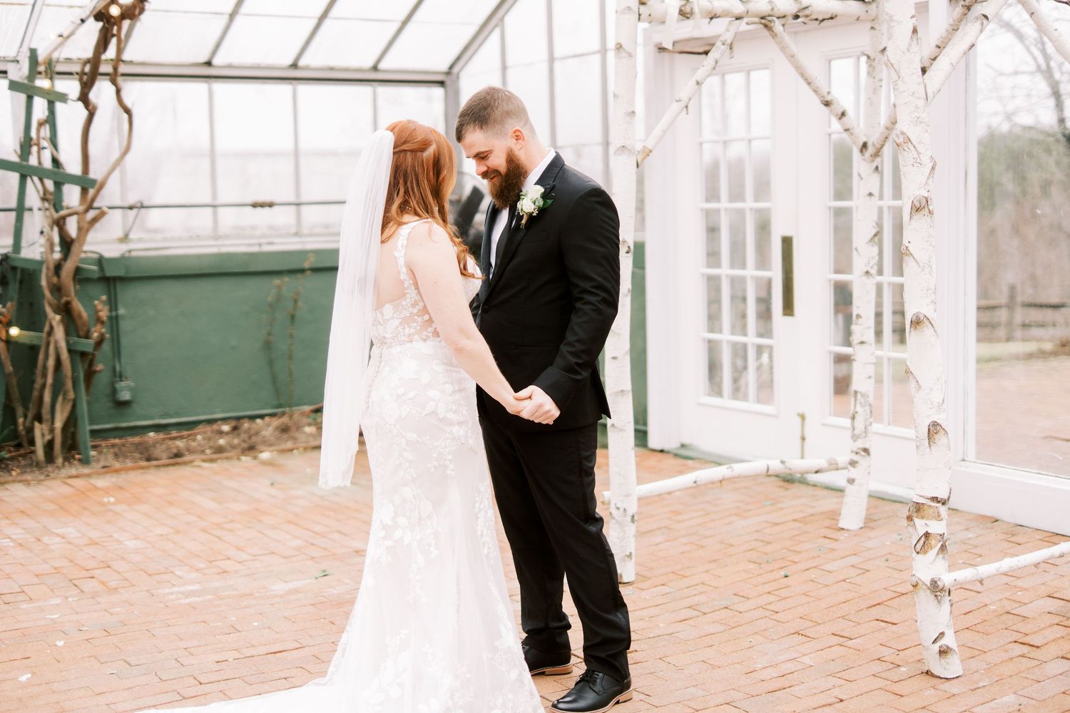 A couple share an intimate moment in a romantic greenhouse venue decorated with white architectural details.