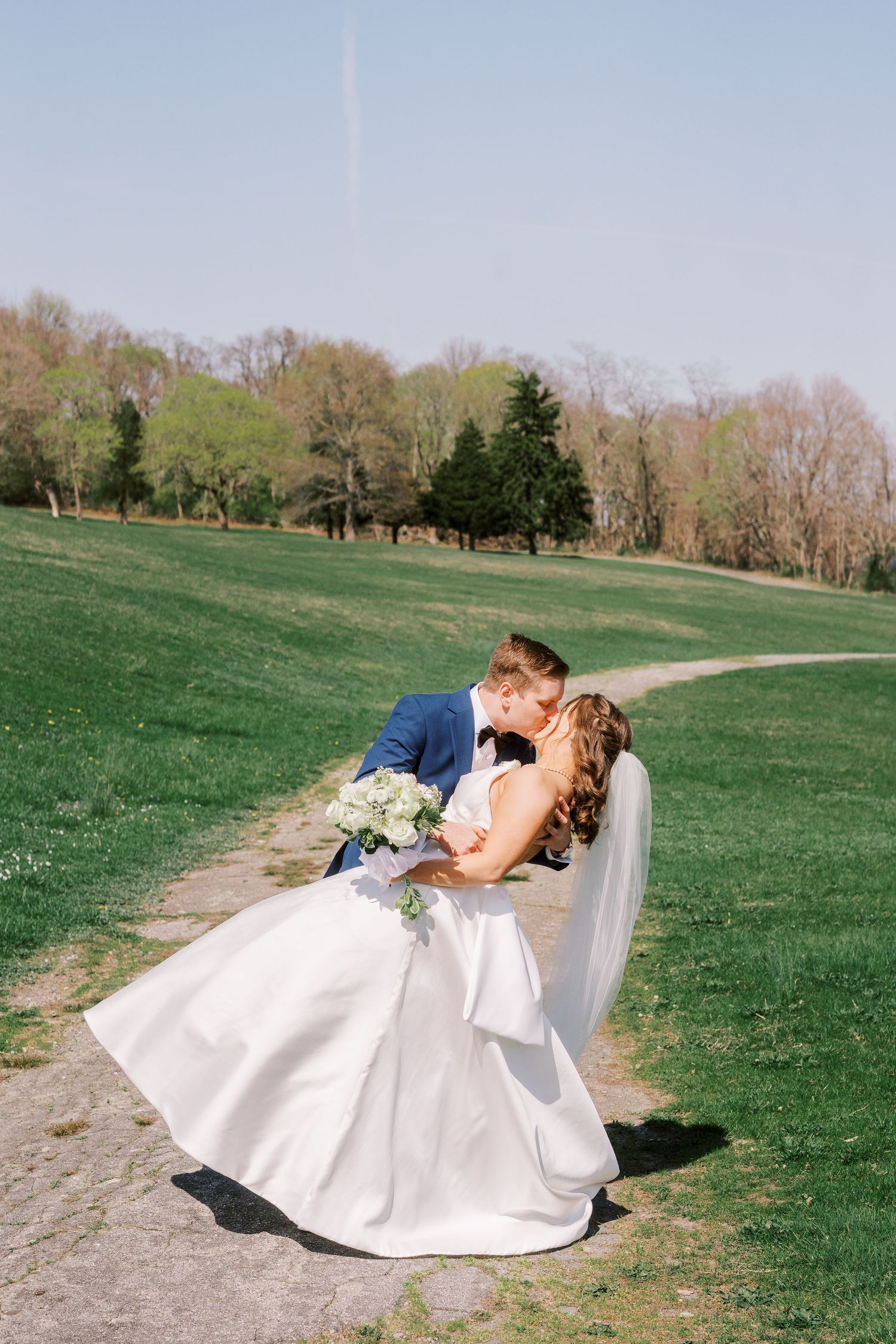 A romantic wedding photo sequence of a couple in white dress and navy suit dipping on a grassy hillside on their special day.