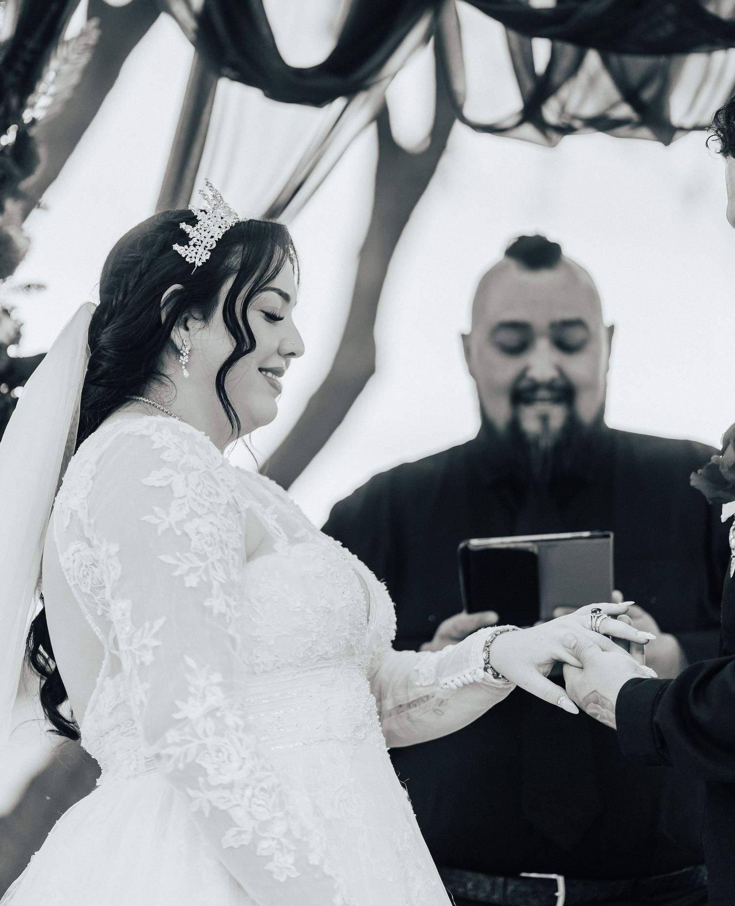 Black and white photo of an elegant bride at a wedding ceremony wearing a white lace dress and delicate crown.