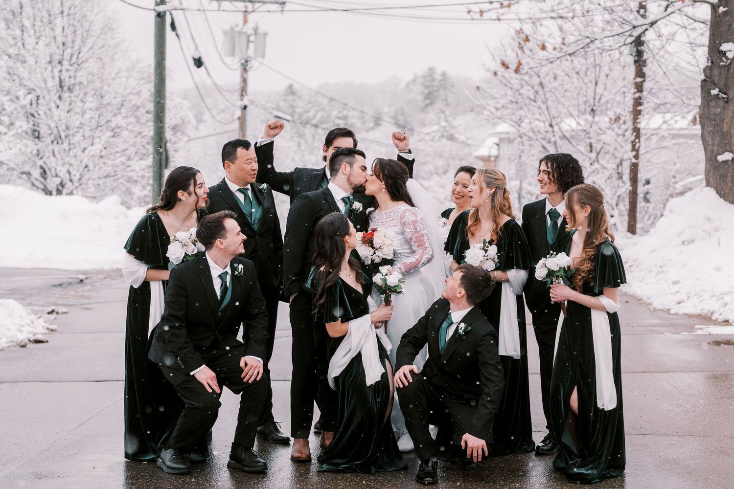 Wedding party in black and white attire posing playfully in snowy winter setting.