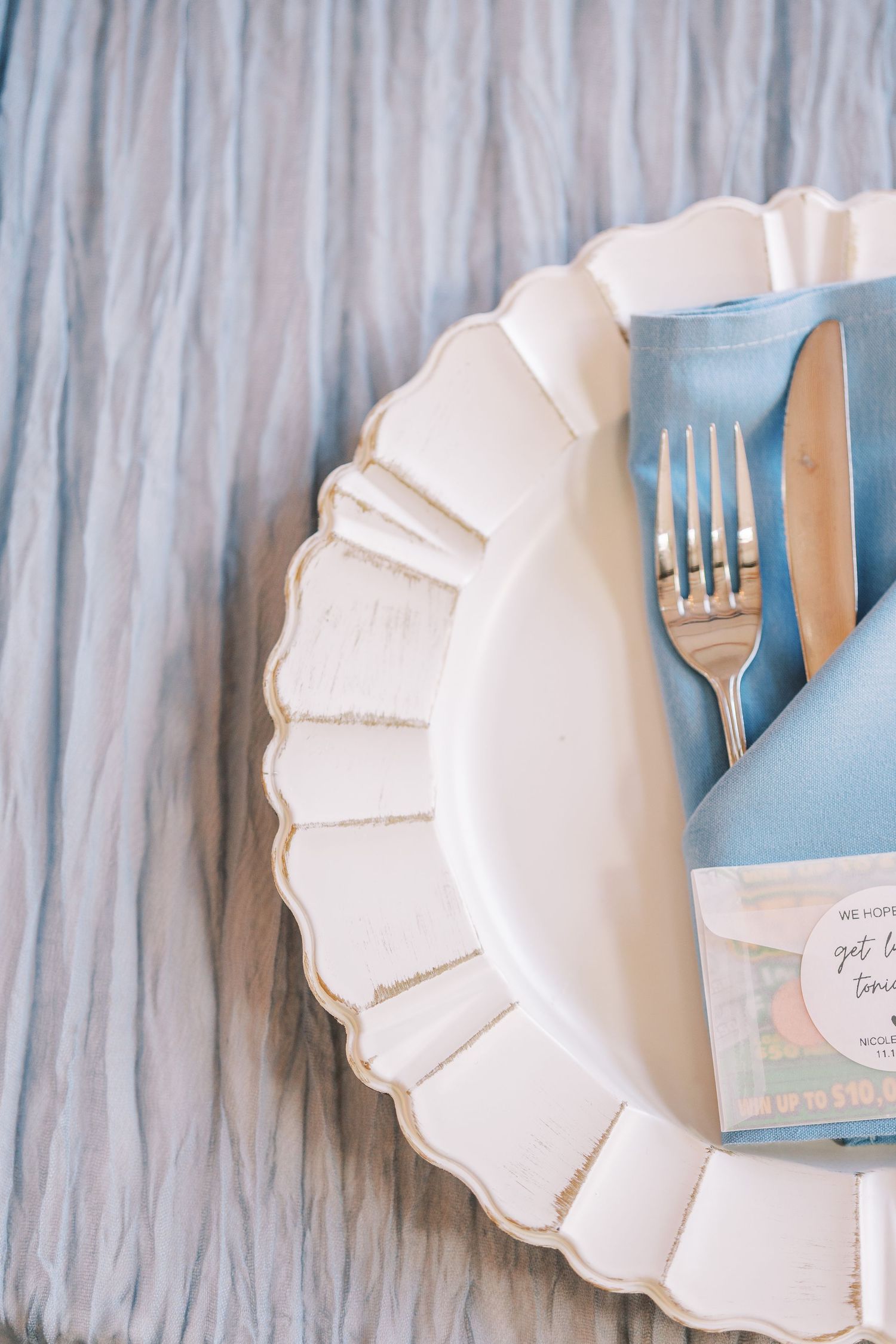 White scalloped ceramic plates and blue napkins arranged in an elegant table setting pattern.