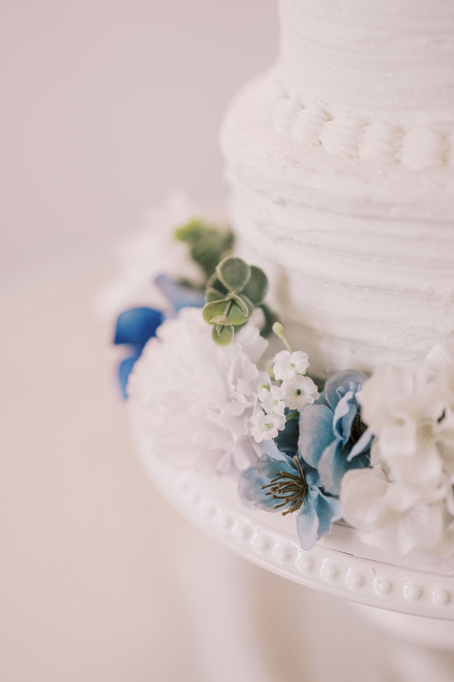 Close-up view of a white wedding cake decorated with delicate blue and white flowers and green accents.