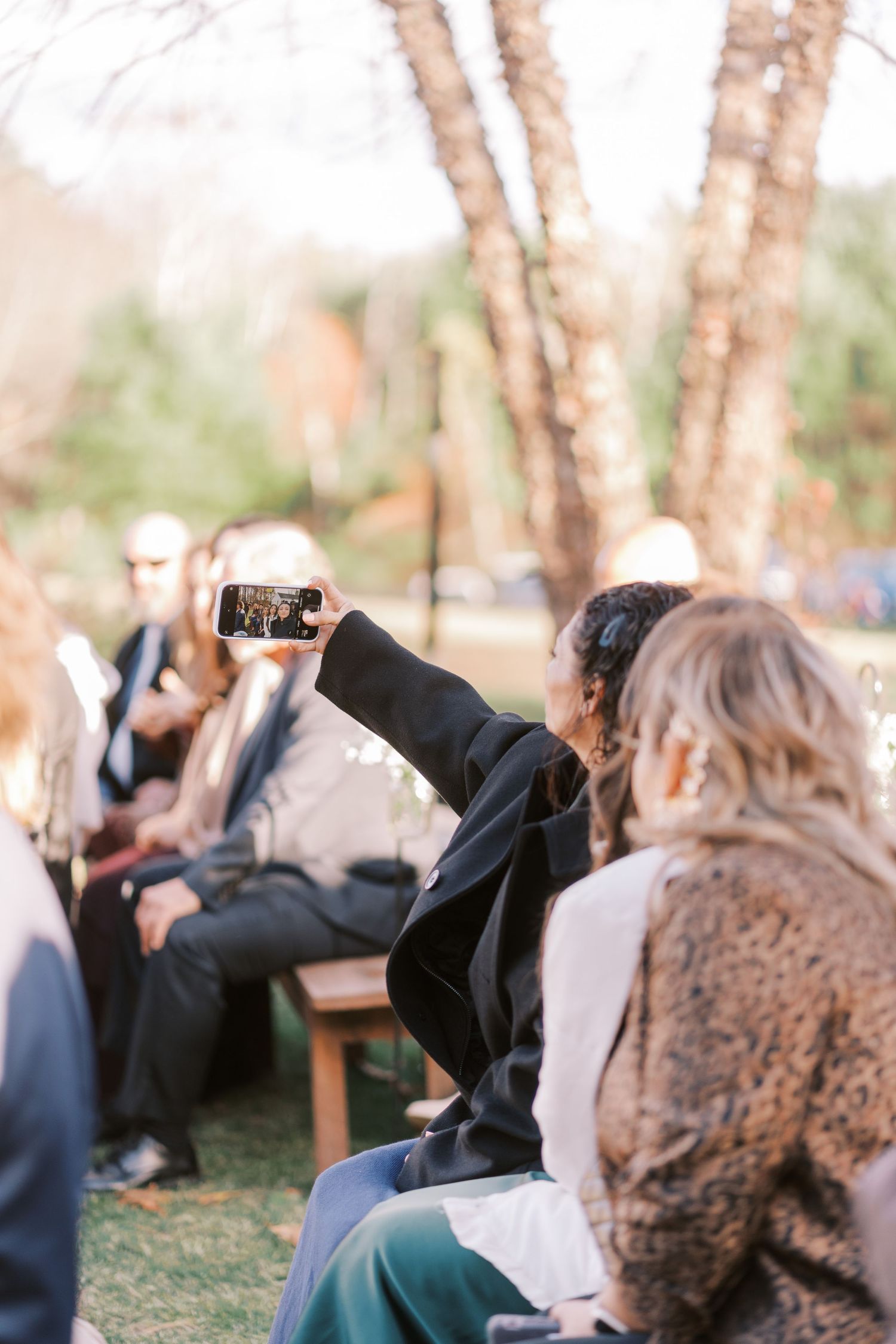 People sitting outdoors at an event while someone holds up a phone to take a photo or video.