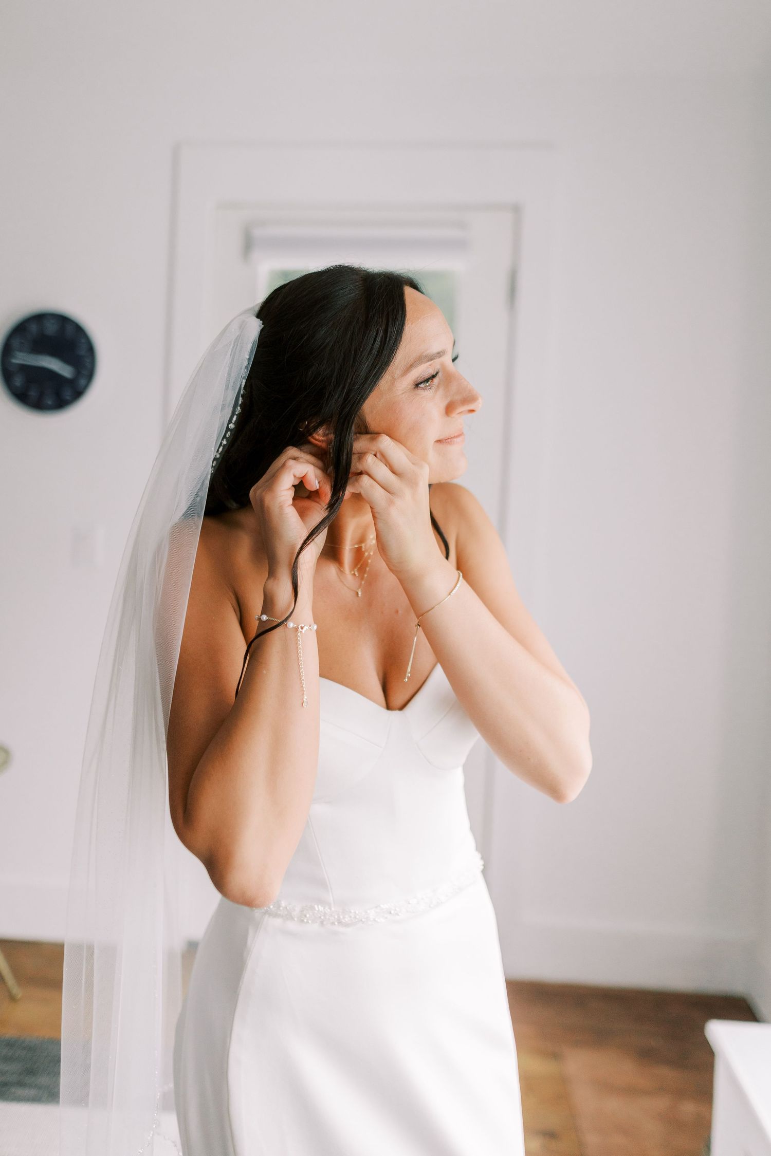 Side profile of bride in white dress putting on jewelry.