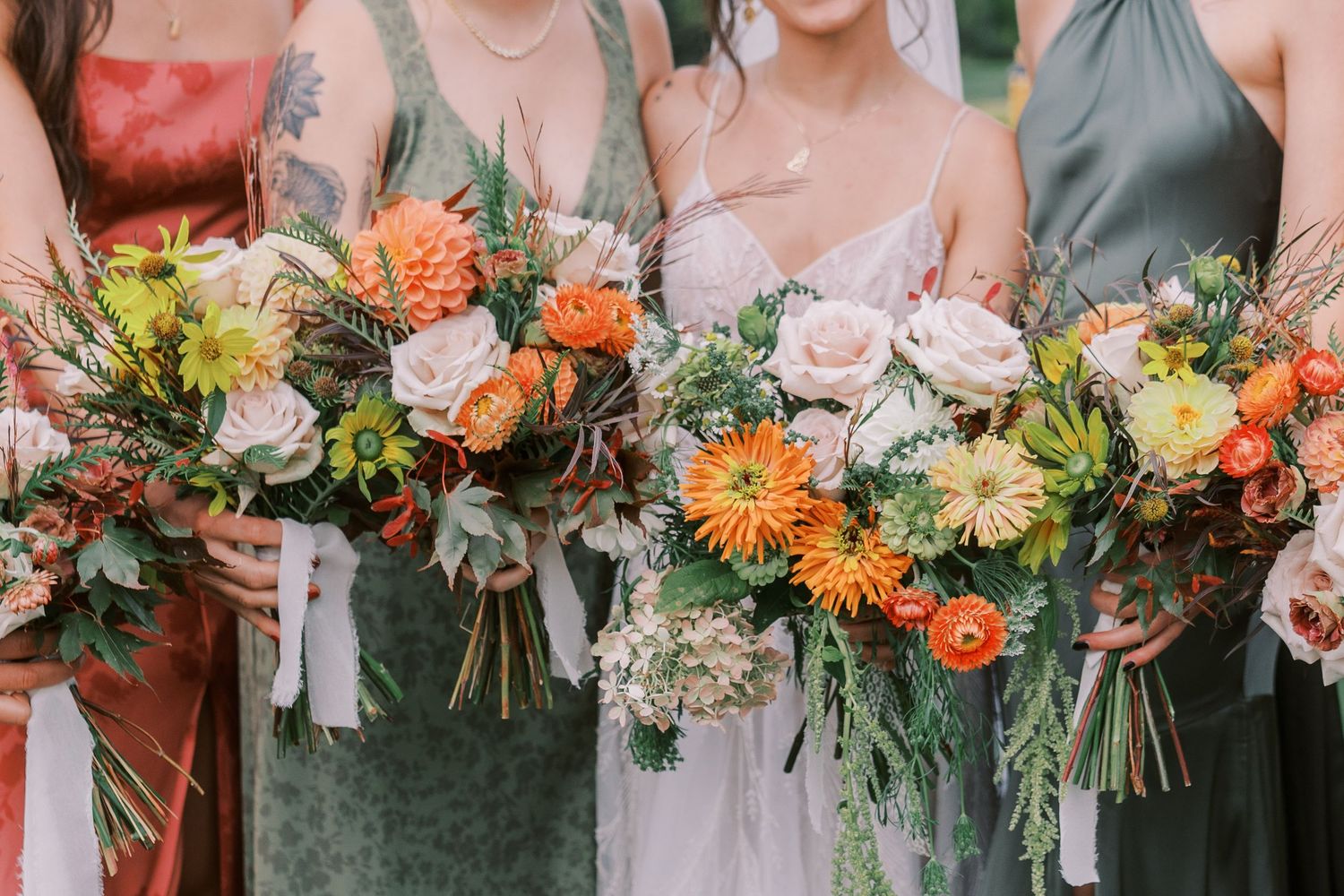 Wedding party members hold vibrant orange and white floral bouquets against gray and blush colored attire.