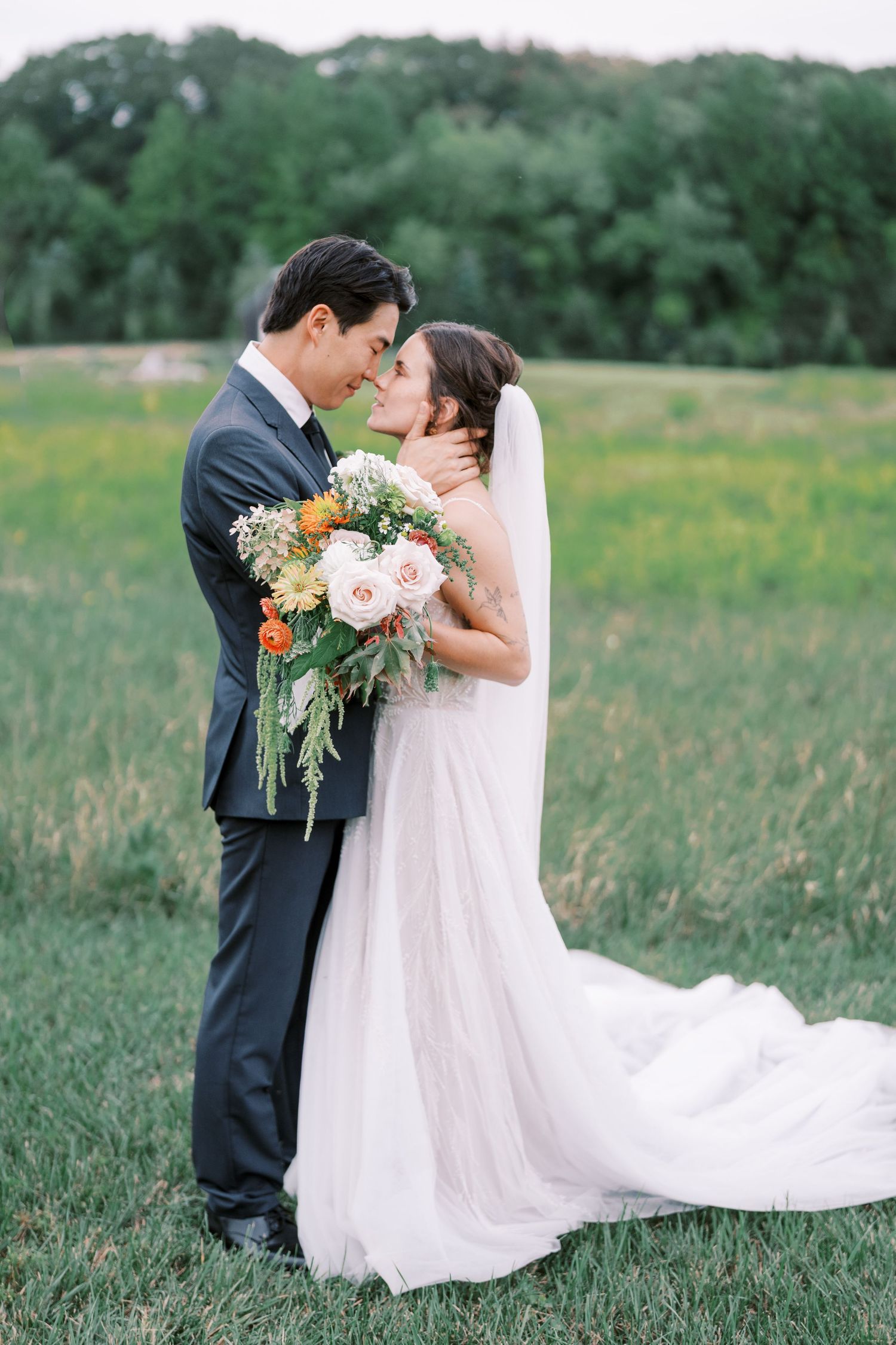 A romantic wedding portrait of a couple embracing in a meadow with the bride holding a beautiful floral bouquet.
