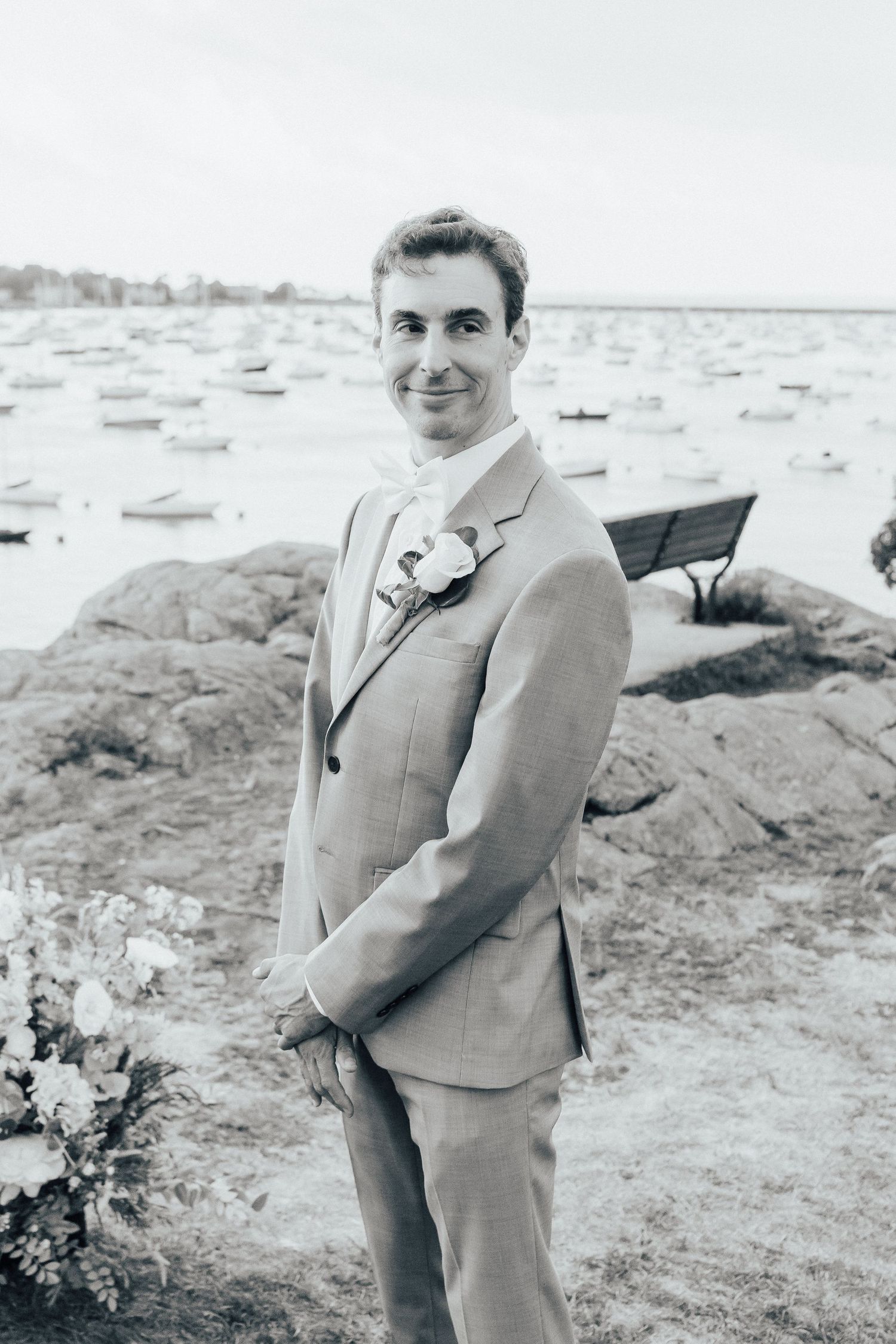 A seaside wedding photoshoot featuring rocky coastal landscape and boats in the background.
