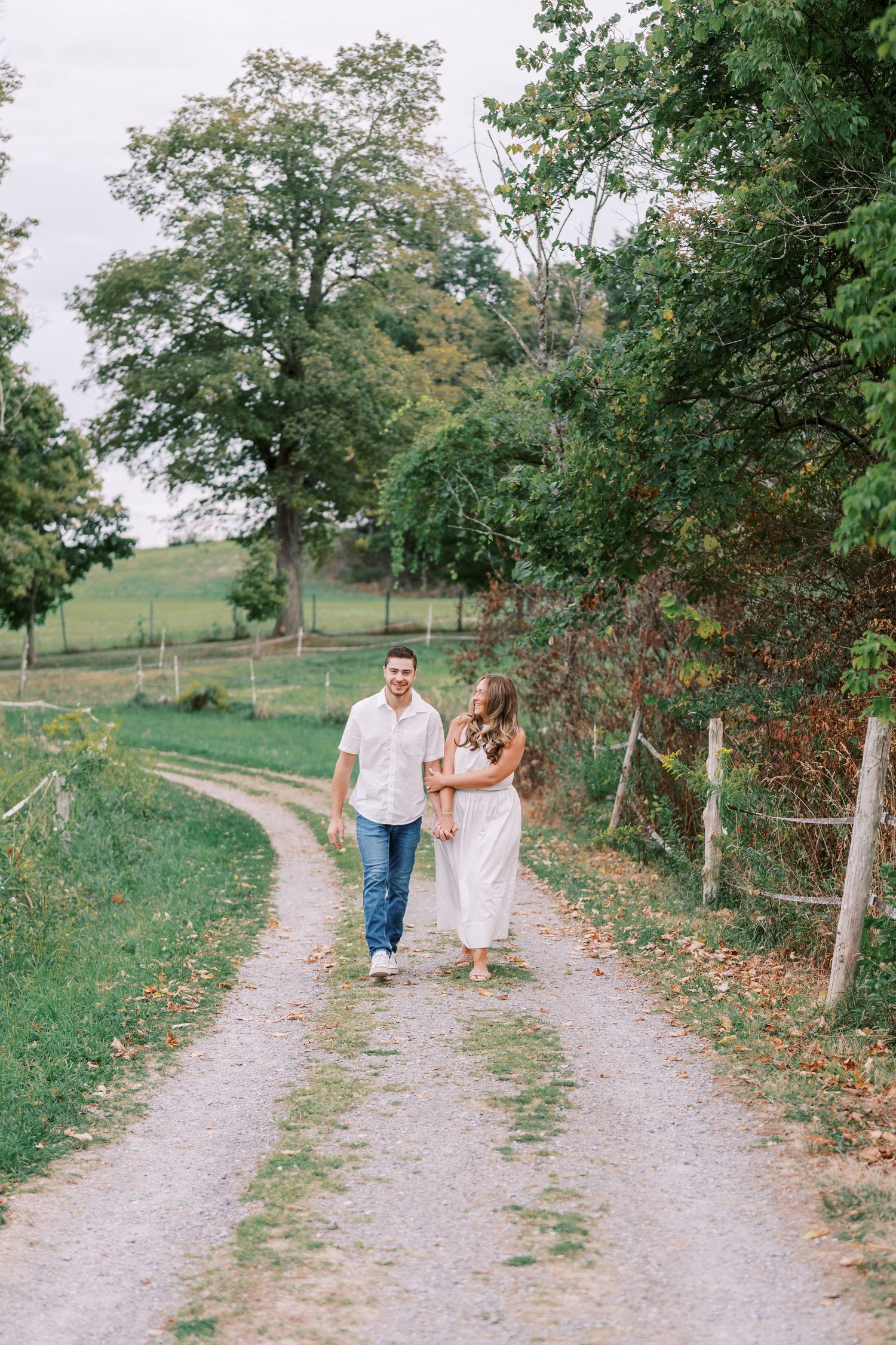 A couple walking hand in hand down a scenic country path surrounded by trees and greenery.
