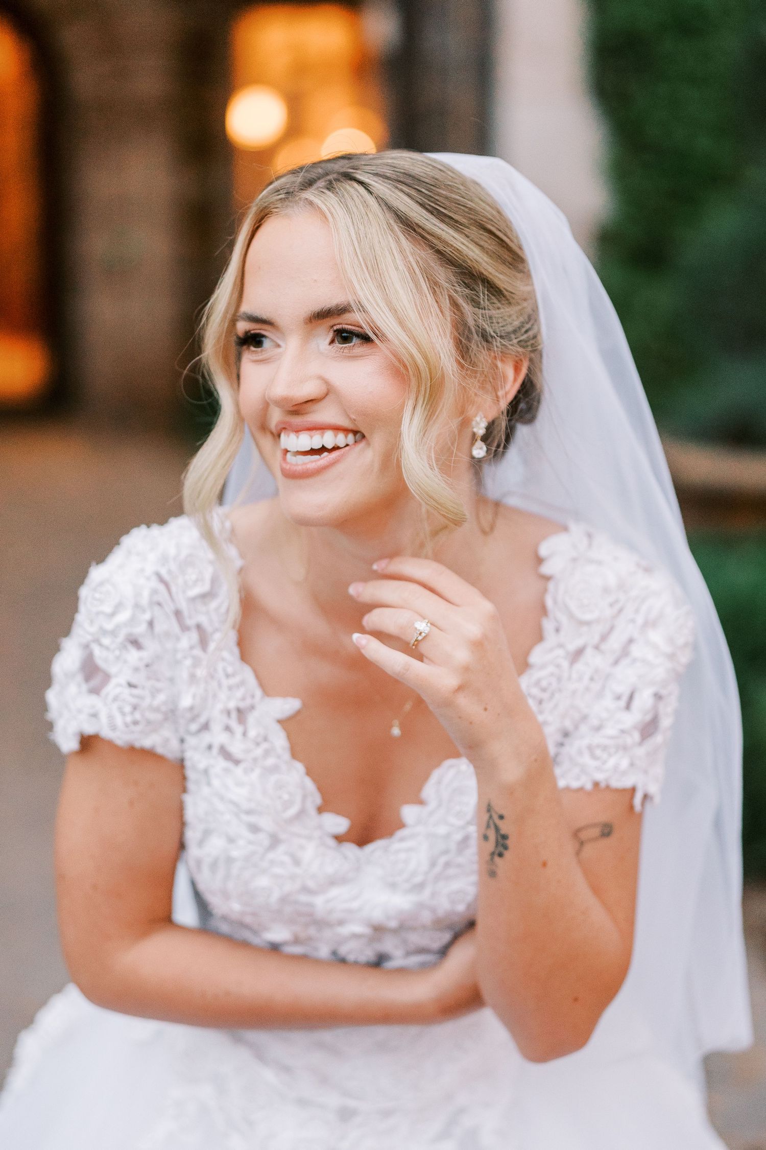 A bride in a white lace wedding dress with a veil laughs joyfully during her wedding photoshoot.