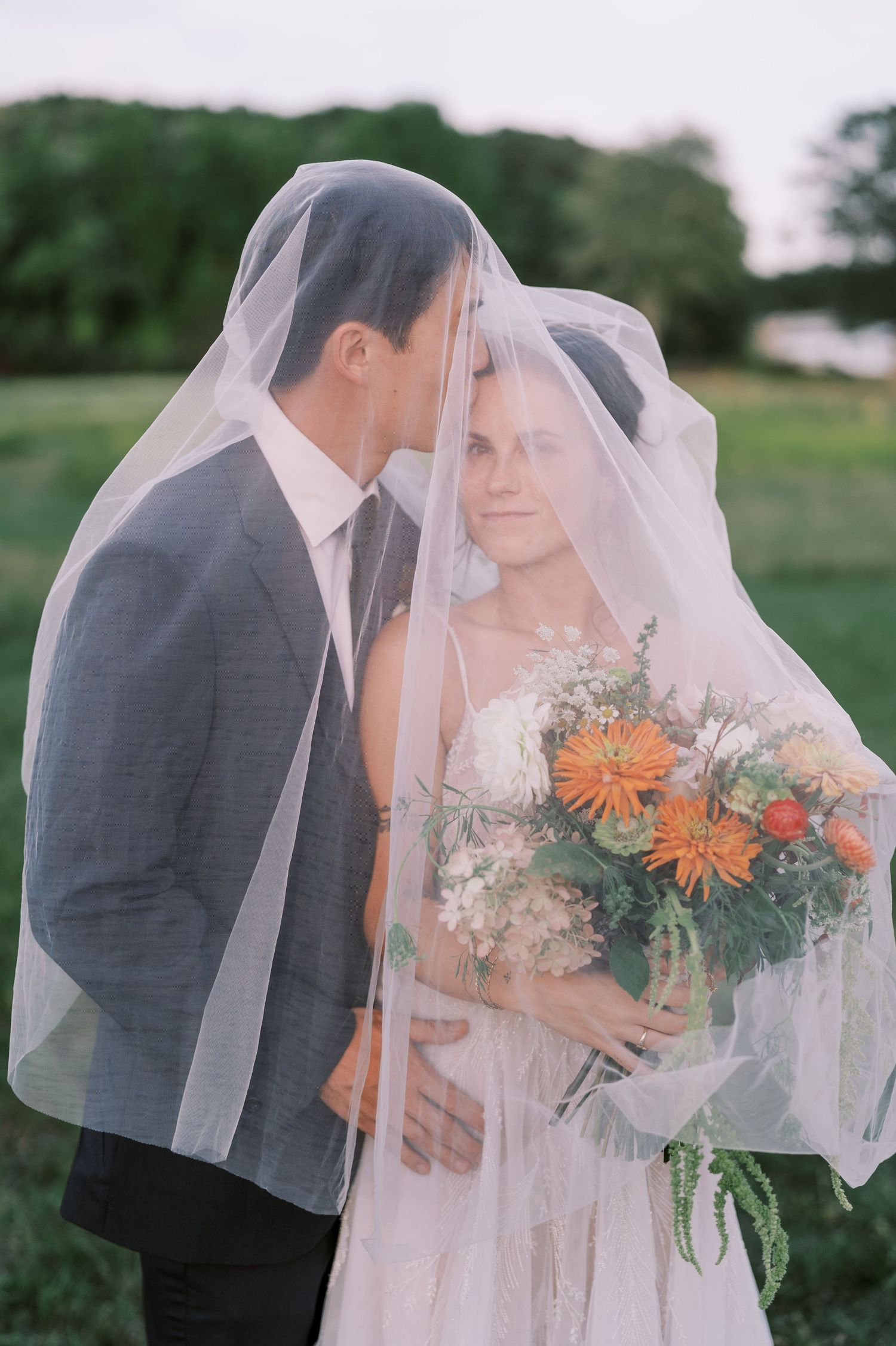 Romantic wedding portraits under veil with orange and white floral bouquet.