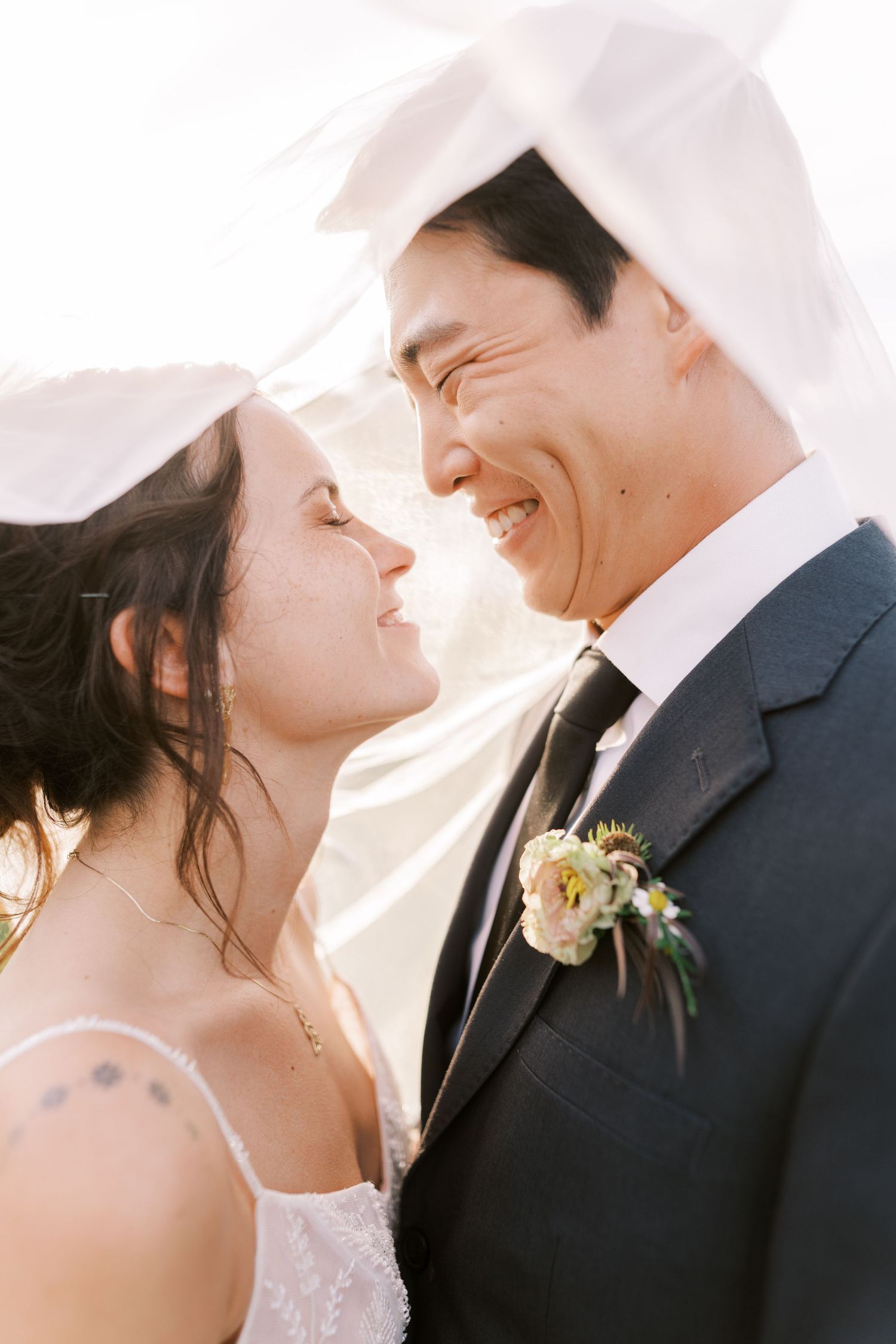 A joyful close-up wedding photo showing a couple sharing a tender moment in bright sunlight.