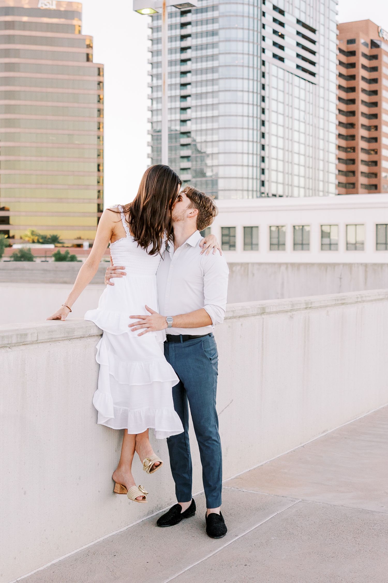 Couple posing together on urban rooftop with city buildings in background.