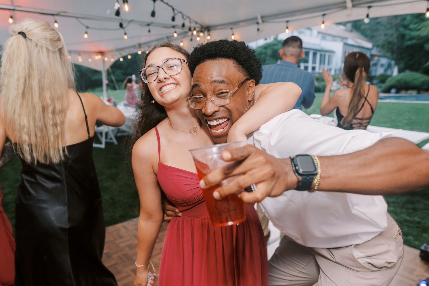 Wedding guests dancing and celebrating at an outdoor reception under string lights.