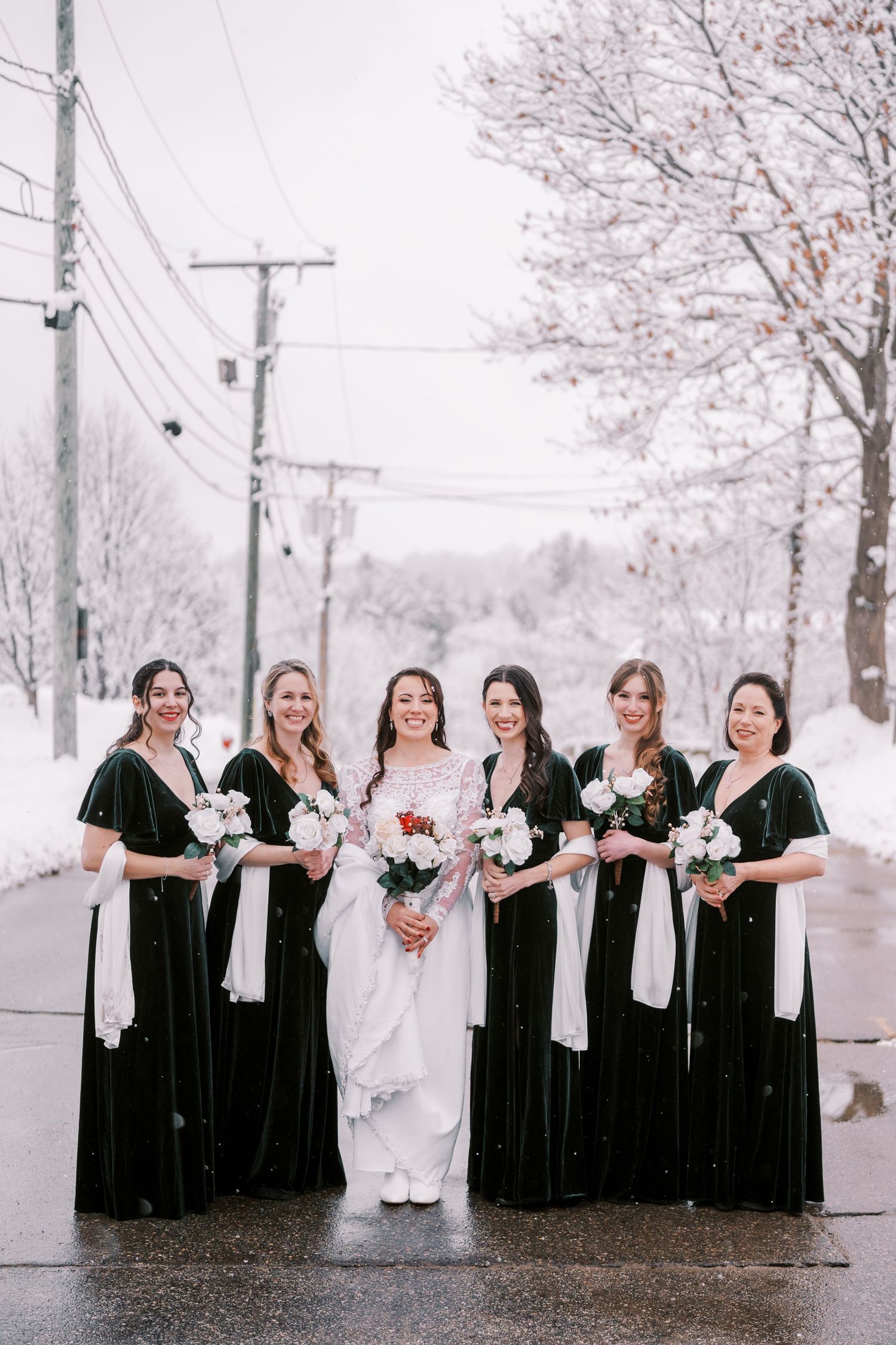 Wedding party poses in winter scene with bridesmaids in dark velvet dresses and white shawls.