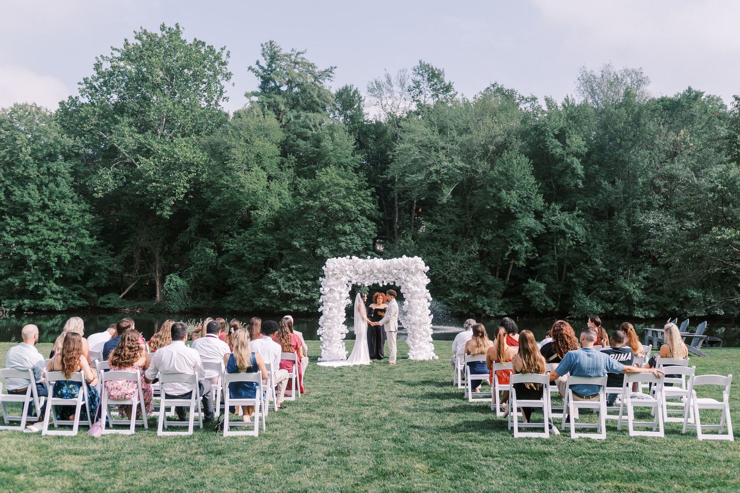 Wide angle view of outdoor wedding ceremony seating with white chairs on grassy lawn.