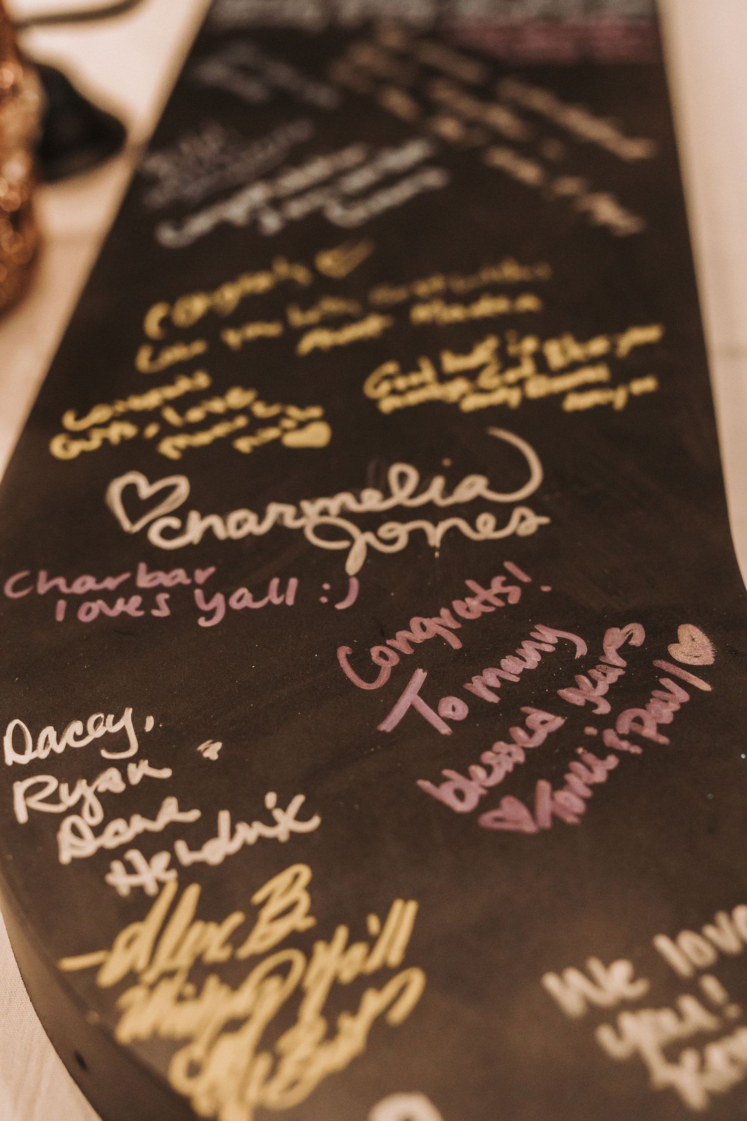 Handwritten signatures and messages in gold and pink ink on a dark surface appear to be from a guest book or signing wall.