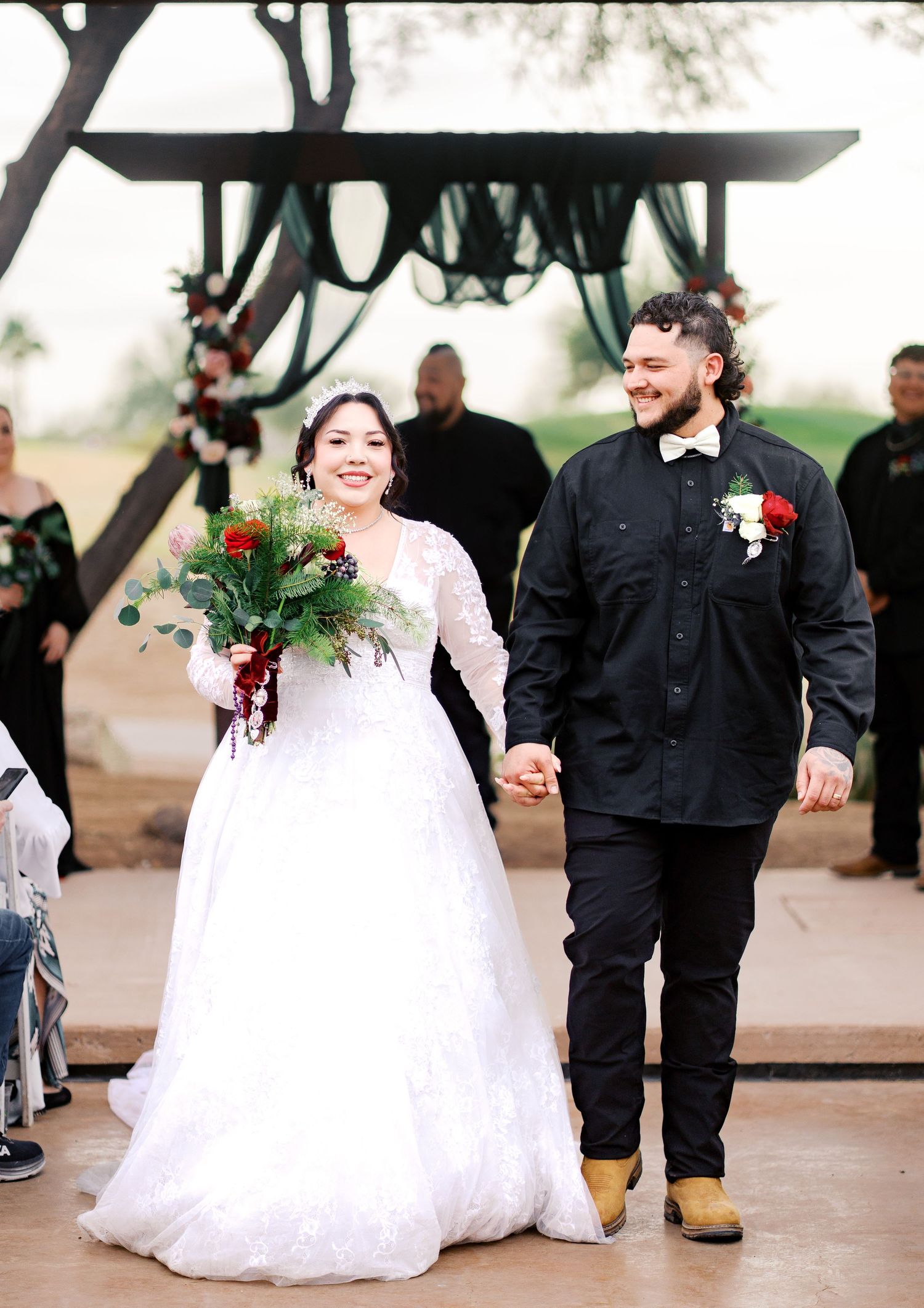 A joyous couple walks hand in hand after their winter wedding ceremony, with bride in white dress and groom in black attire.