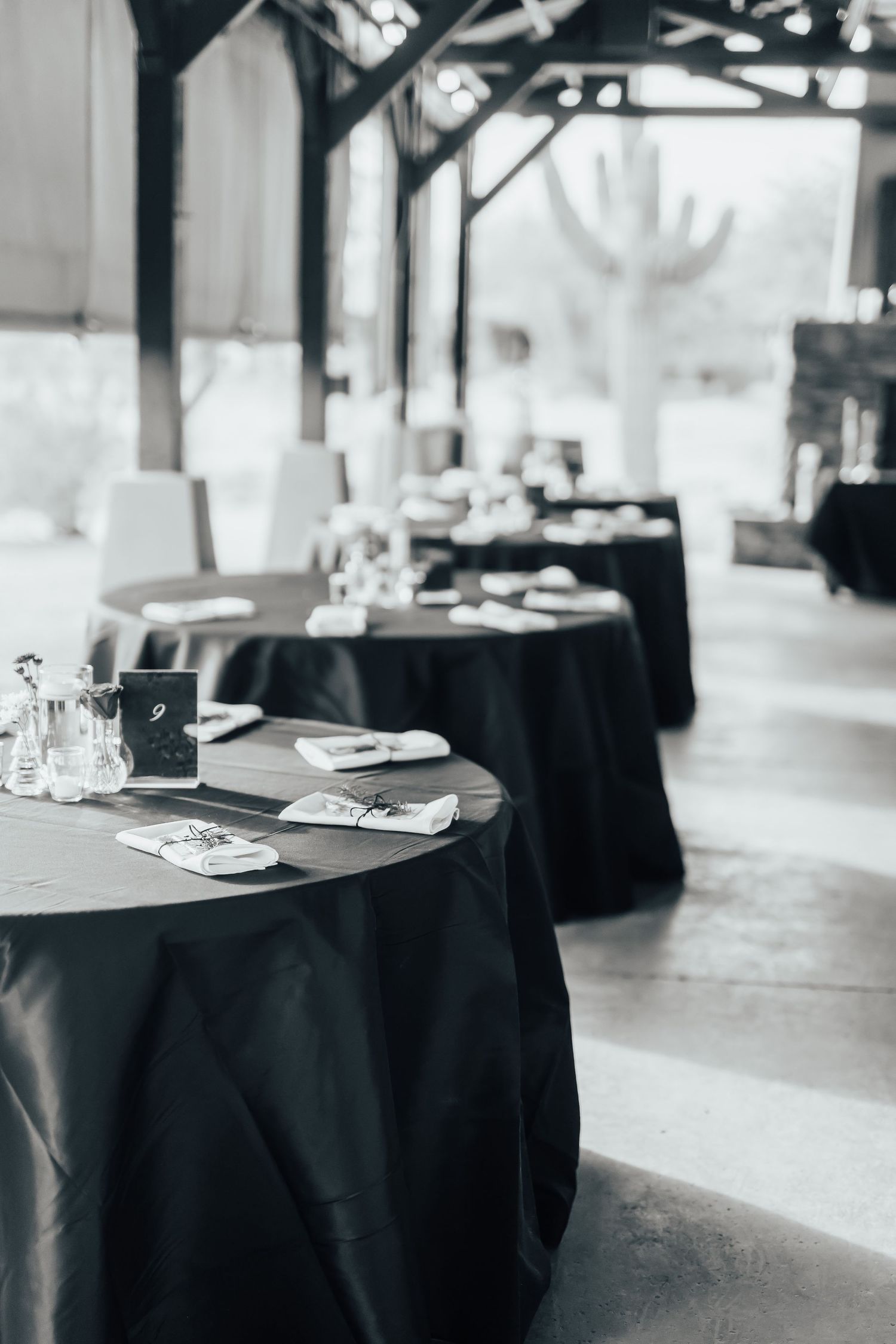 Black tablecloths cover round tables set for an elegant event with place settings and glassware in muted lighting.