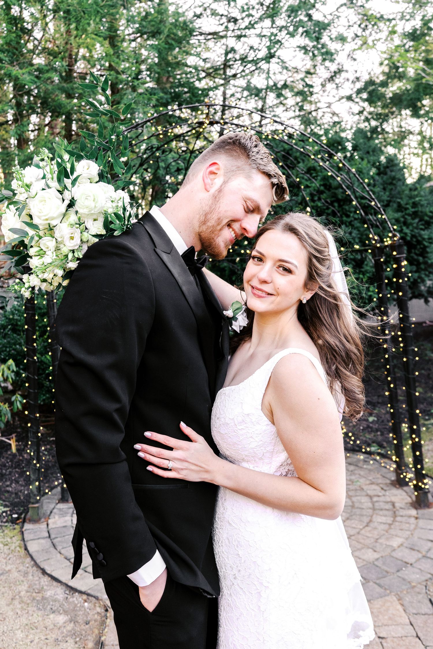 Happy couple embraces and shares a joyful moment on a garden pathway with twinkle lights.