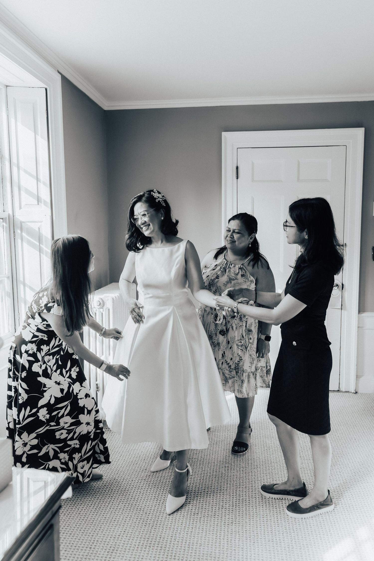 Black and white photo sequence showing people helping with a wedding dress fitting in a bright room.