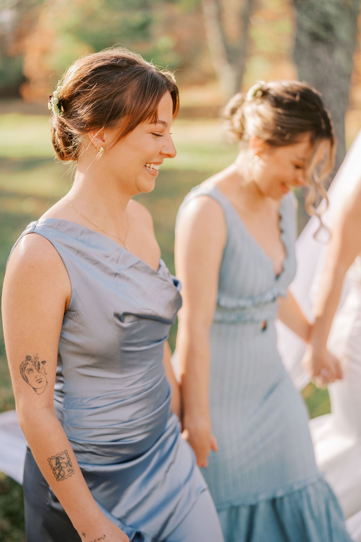 Bridesmaids in soft blue dresses smile during an outdoor wedding celebration in autumn.