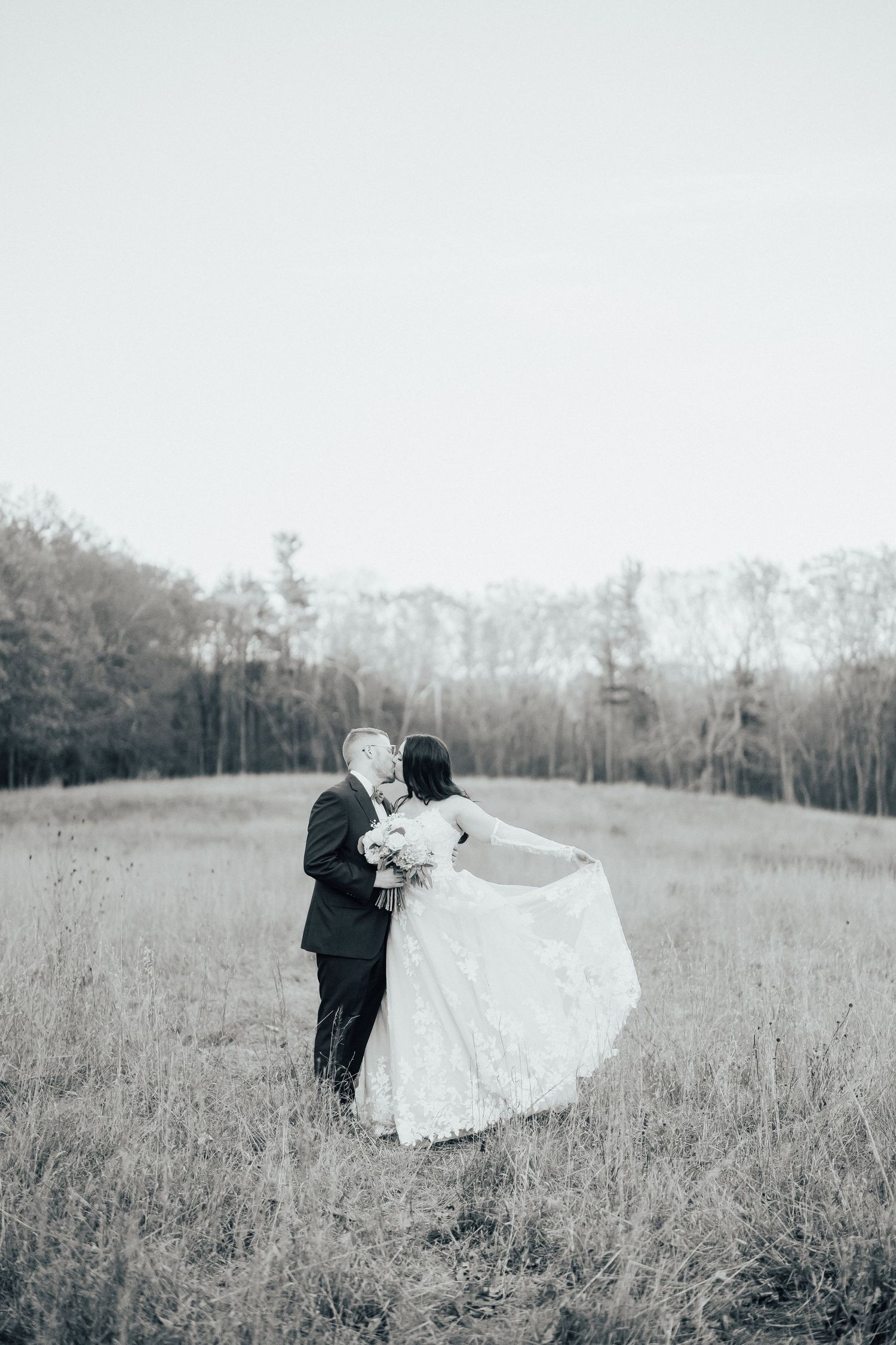 A couple in formal wedding attire embraces in a serene meadow field on their special day.